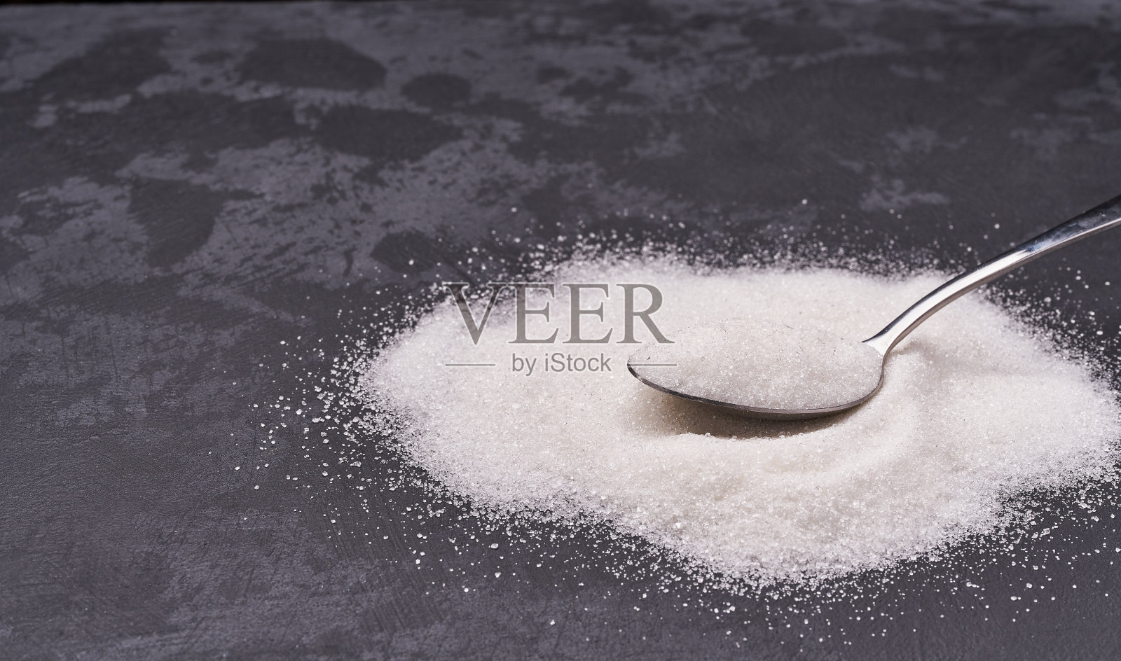 糖粉放在金属勺子里，黑色背景。照片摄影图片