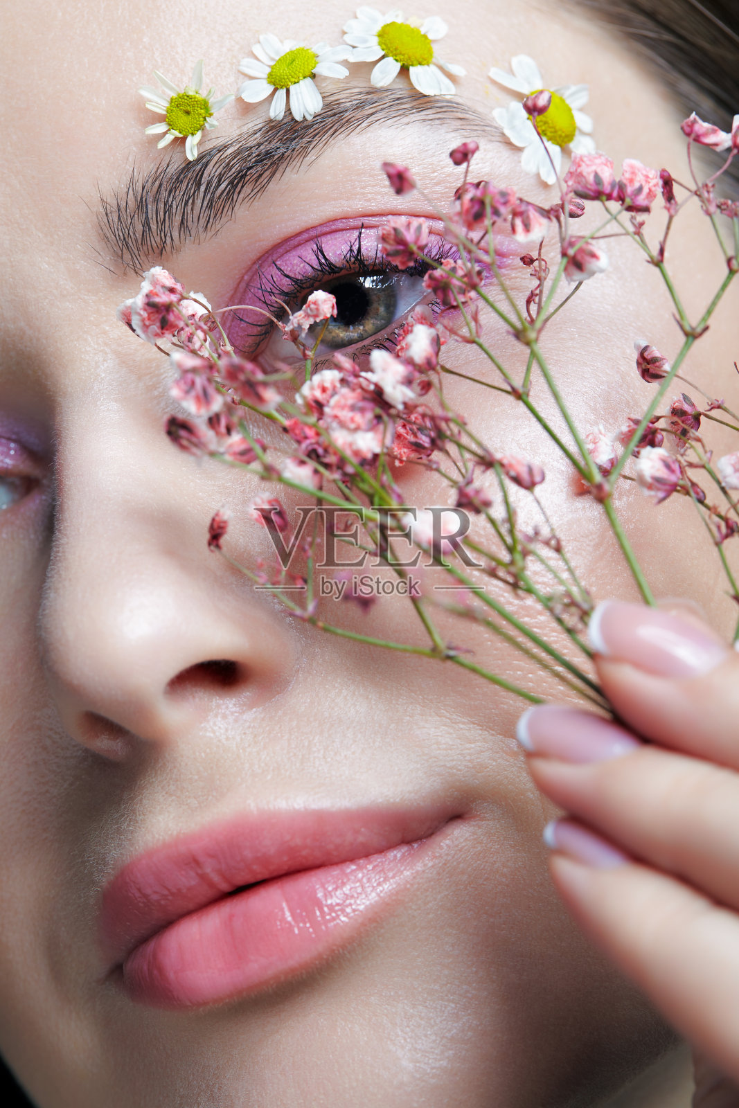 女性的脸，粉色的妆容。一名女子，手里拿着凤仙花，近脸。眉毛上点缀着小的洋甘菊花。照片摄影图片