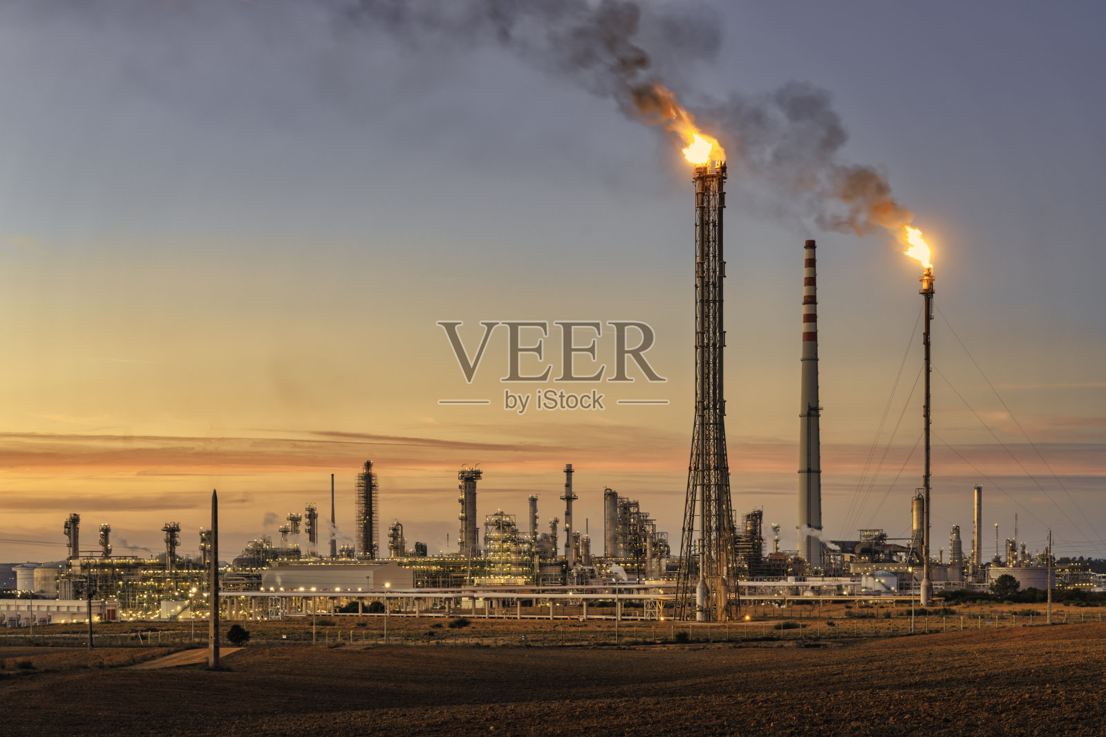 日落时分的葡萄牙Sines精炼厂，烟囱里冒出火焰和烟雾。照片摄影图片