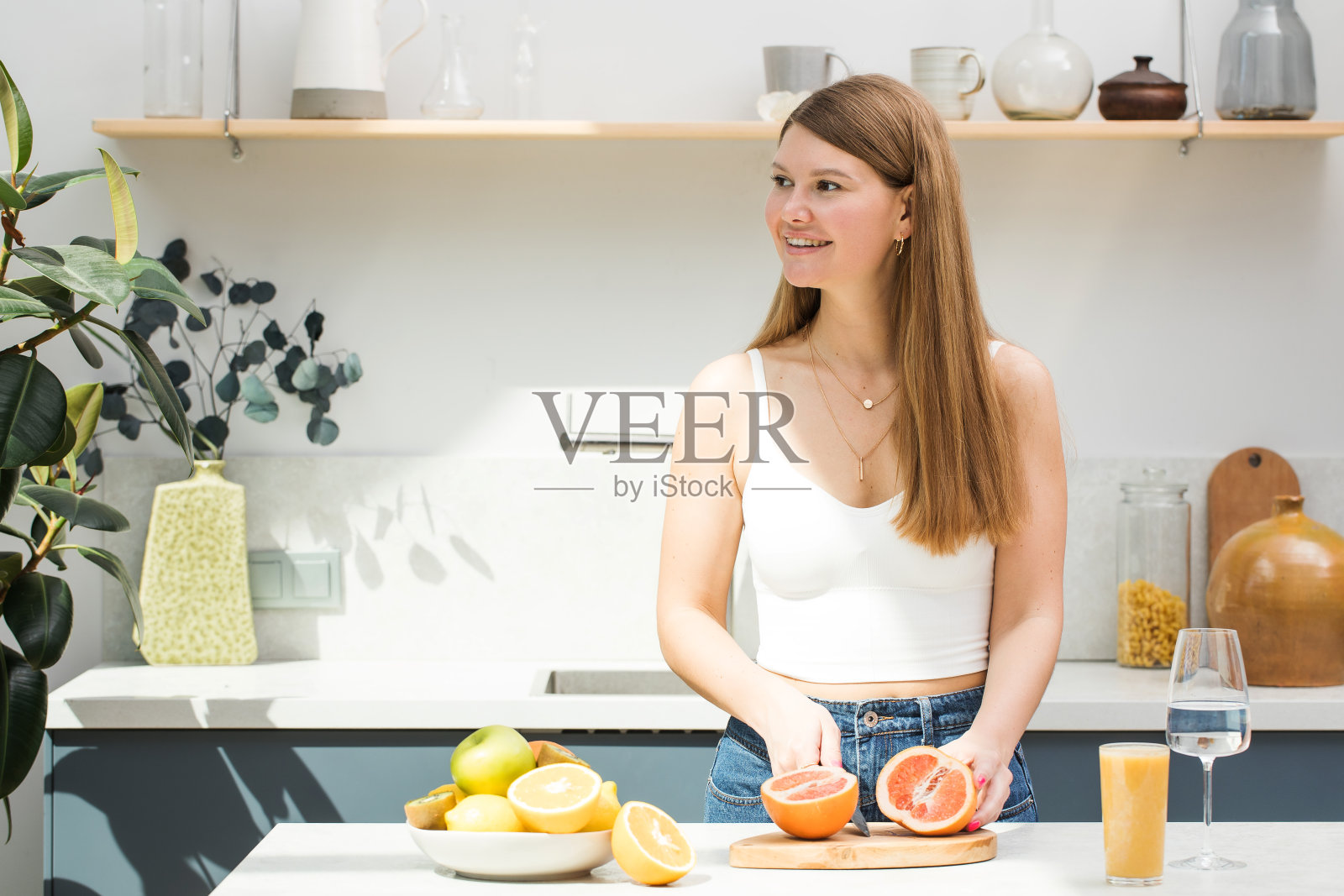 迷人的年轻女子微笑着在厨房切水果。照片摄影图片