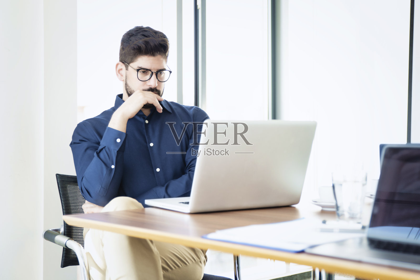 在办公室工作时坐在笔记本电脑后面思考的商人的镜头照片摄影图片