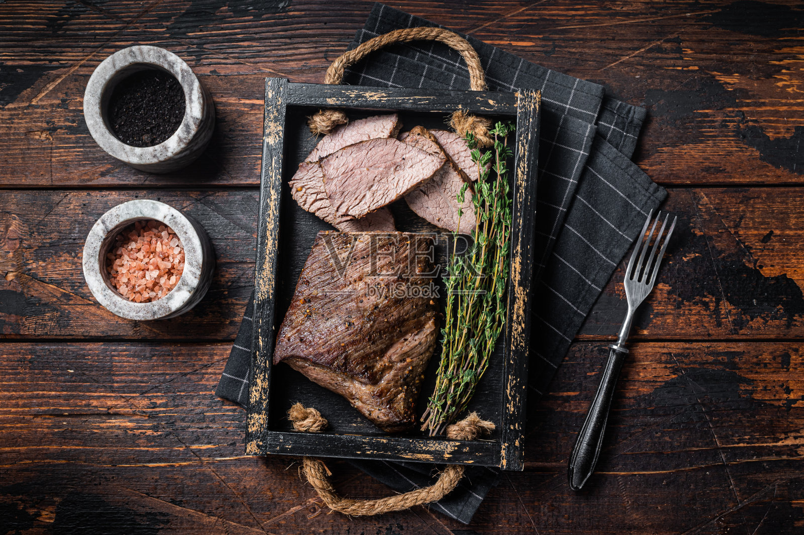 烤三尖牛排，西冷牛肉，用香草放在托盘里。木制背景。俯视图照片摄影图片