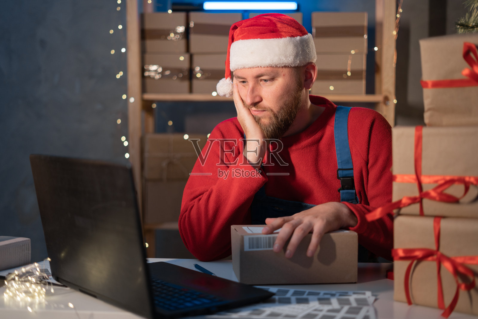 启动。抑郁,压力。年轻的圣诞老人用笔记本电脑和送货包装盒在桌子上，小企业主在家里办公，中小企业，圣诞购物网上照片摄影图片