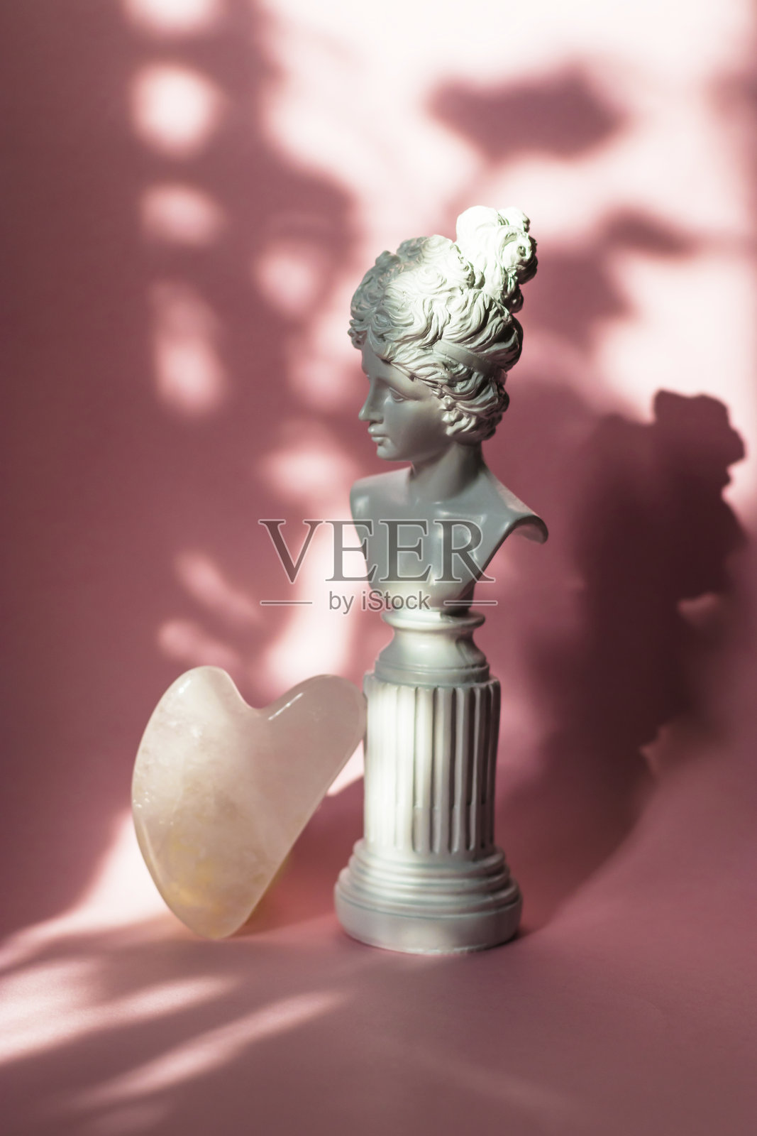 粉粉石英石在粉彩粉色的背景上做的面部按摩水粉。居家水疗护理理念，美容葆青春，抗衰老治疗。女性胸部有硬硬的阴影照片摄影图片