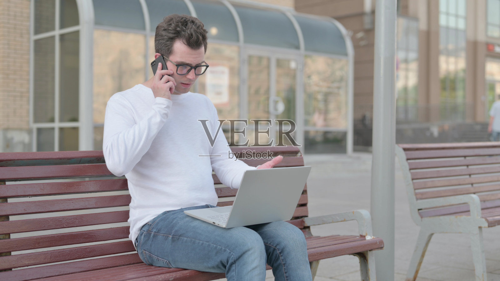 愤怒的年轻人坐在户外长凳上打电话和使用笔记本电脑照片摄影图片