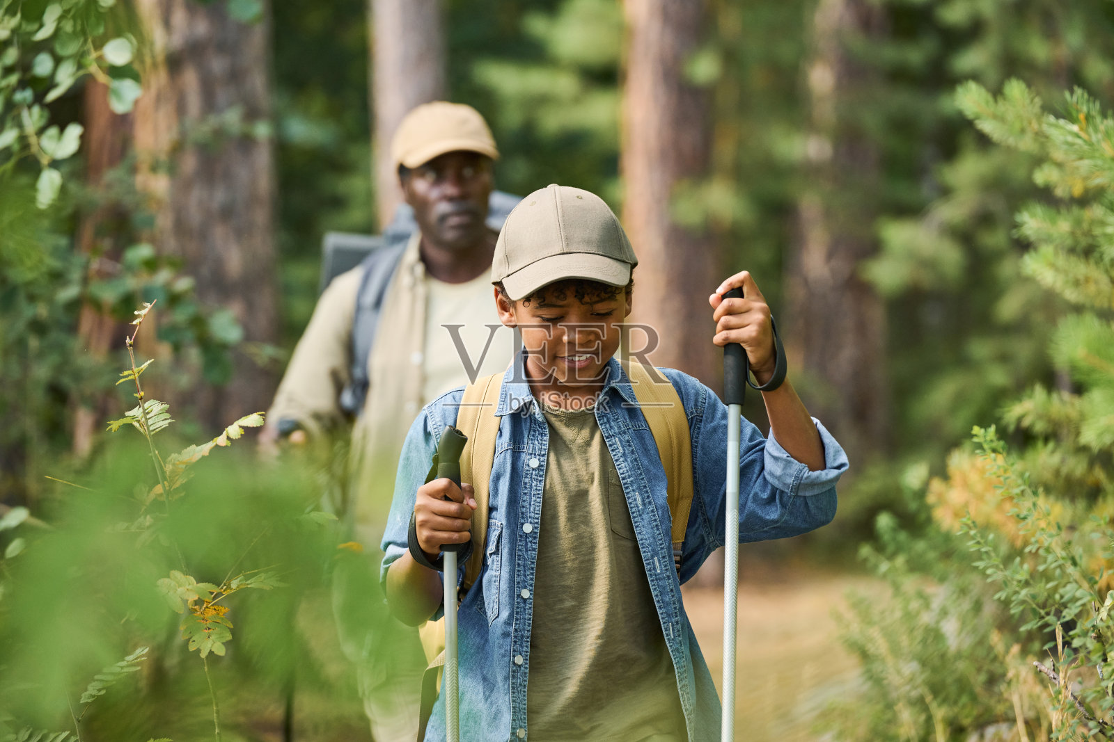 微笑着的年轻男孩拿着拐杖在森林里的步道上行走照片摄影图片
