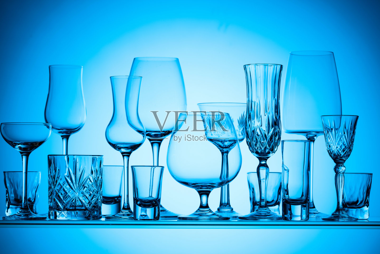 蓝色背景上不同的空玻璃杯。照片摄影图片