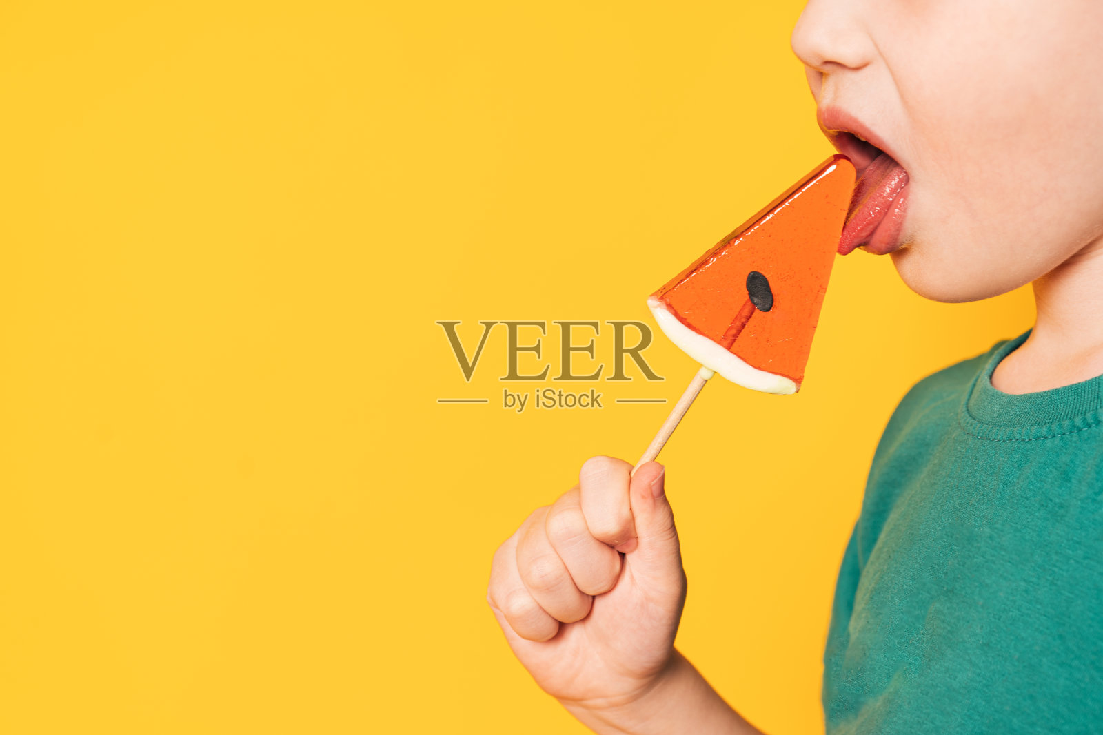 穿着绿色t恤的男孩舔着西瓜形状的棒棒糖照片摄影图片