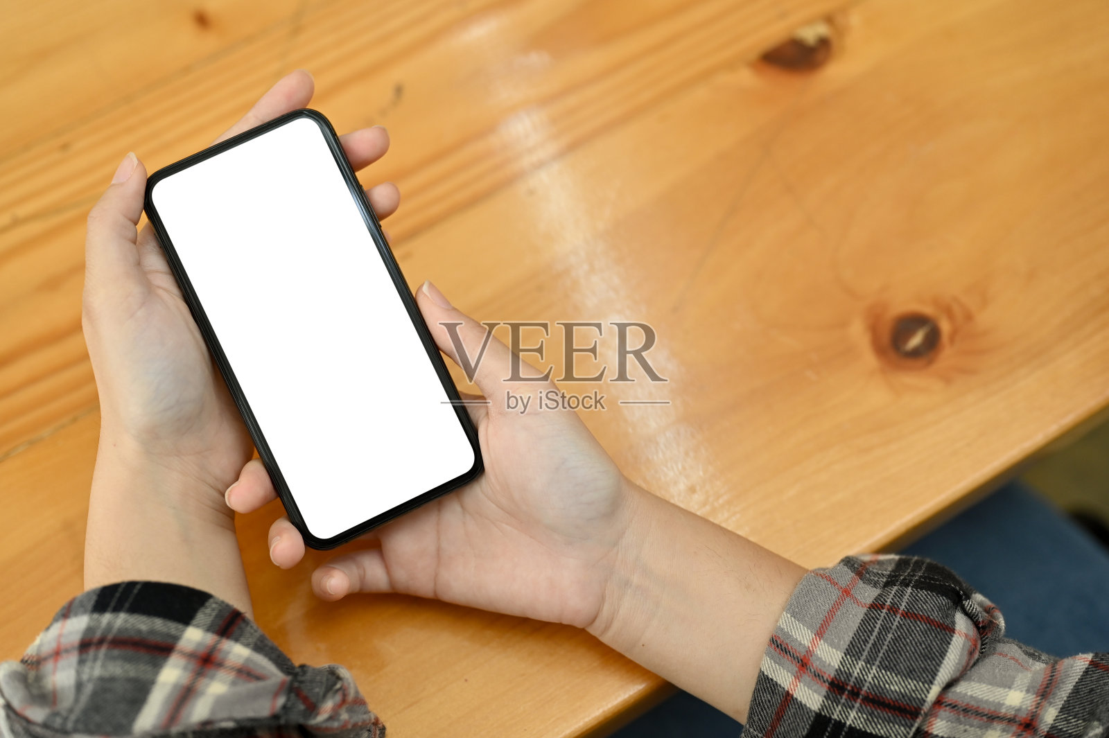 一位时髦的女性在木桌前使用手机。手机白屏模型照片摄影图片