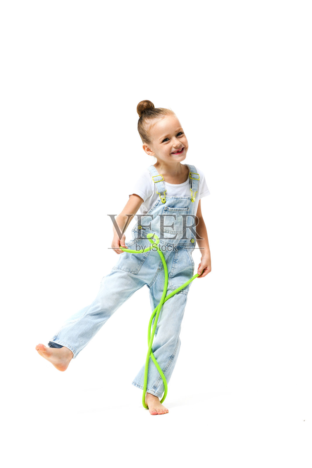 小女孩穿着牛仔工装裤，白色背景上有跳绳。照片摄影图片
