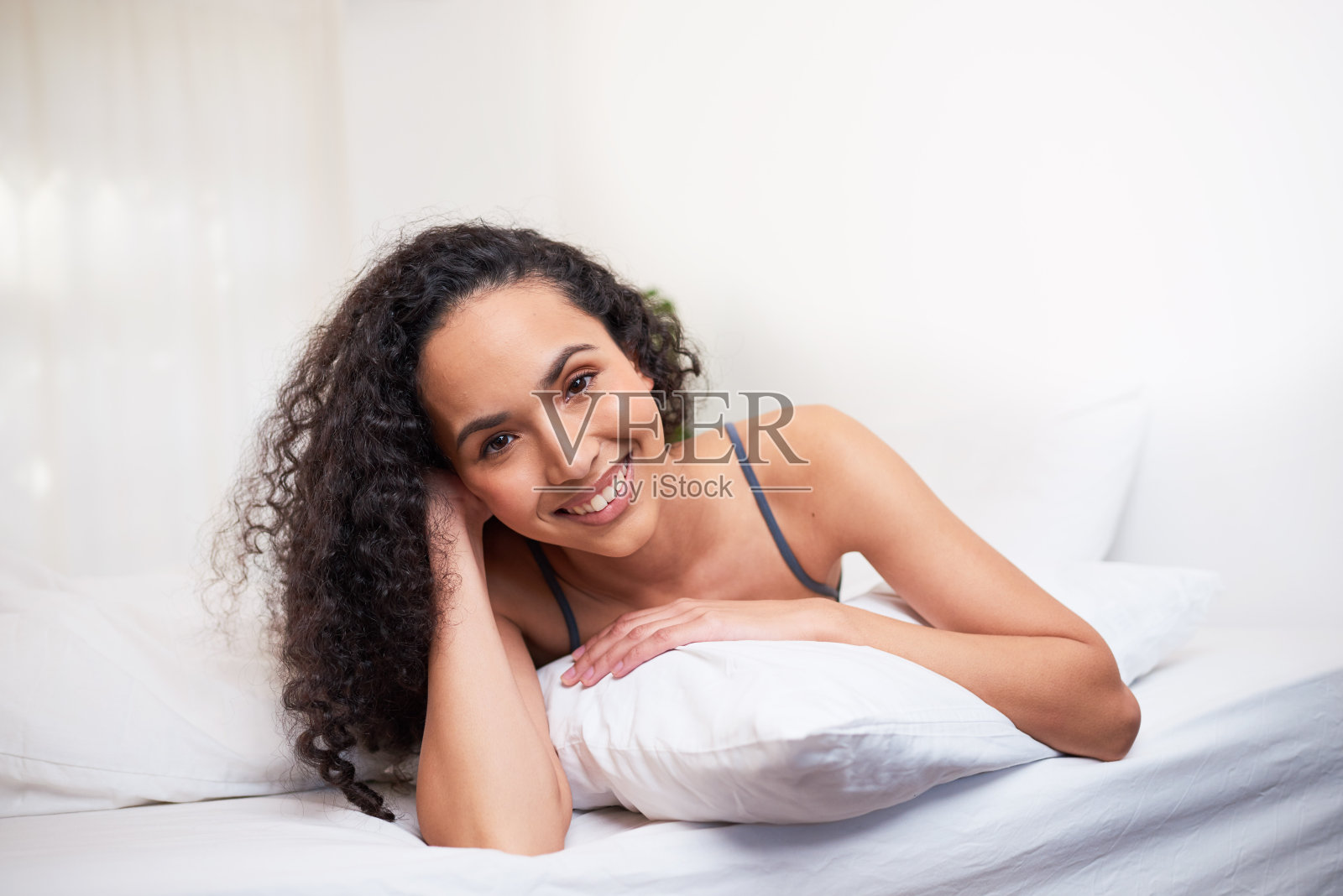 一个美丽的年轻女子趴在床上的枕头上，微笑着，幸福的照片摄影图片