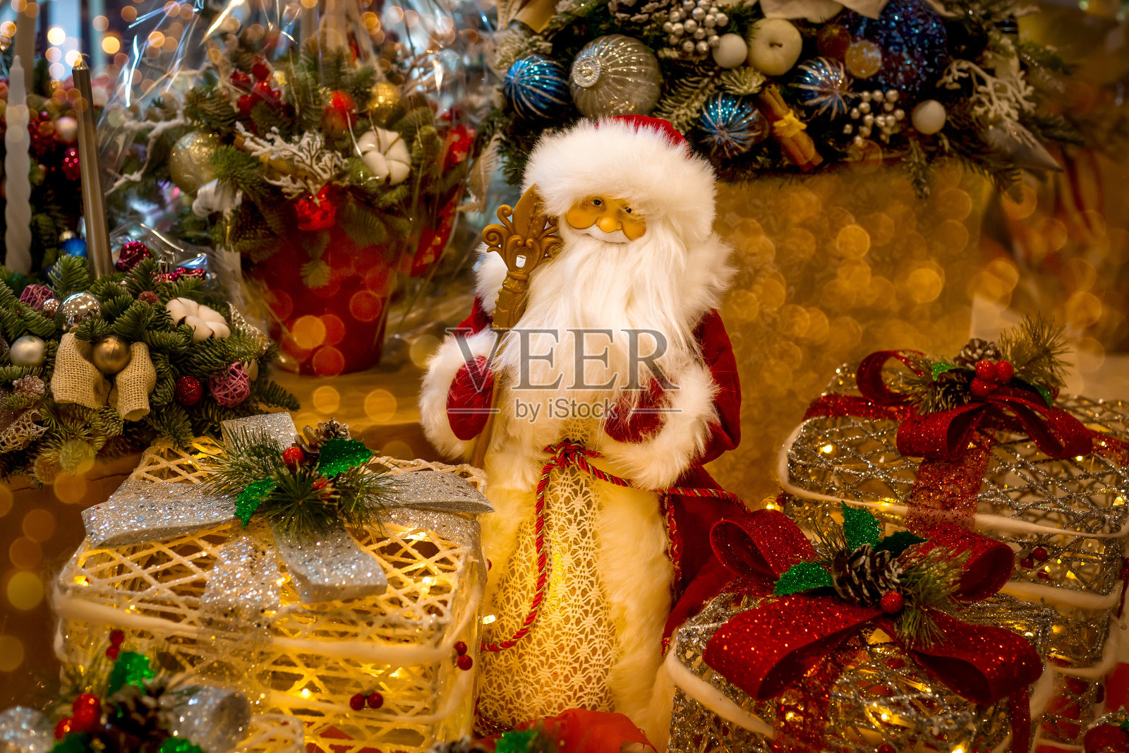 圣诞老人玩偶穿着红色的毛皮大衣，戴着一根手杖和胡子，背景是圣诞装饰的盒子，里面装着圣诞礼物，有圣诞树、蜡烛、球果、球。新年和圣诞节的童话故事照片摄影图片