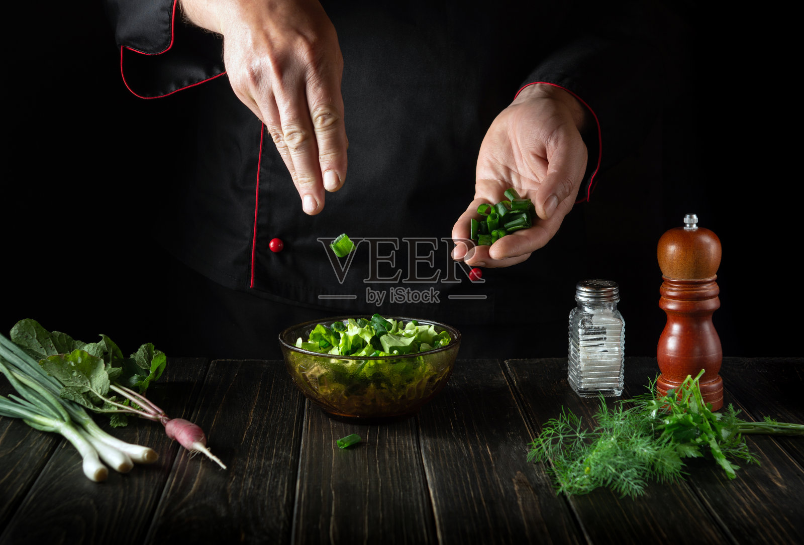 在新鲜蔬菜沙拉中加入切碎的青葱。厨师正在厨房里做美味的食物照片摄影图片