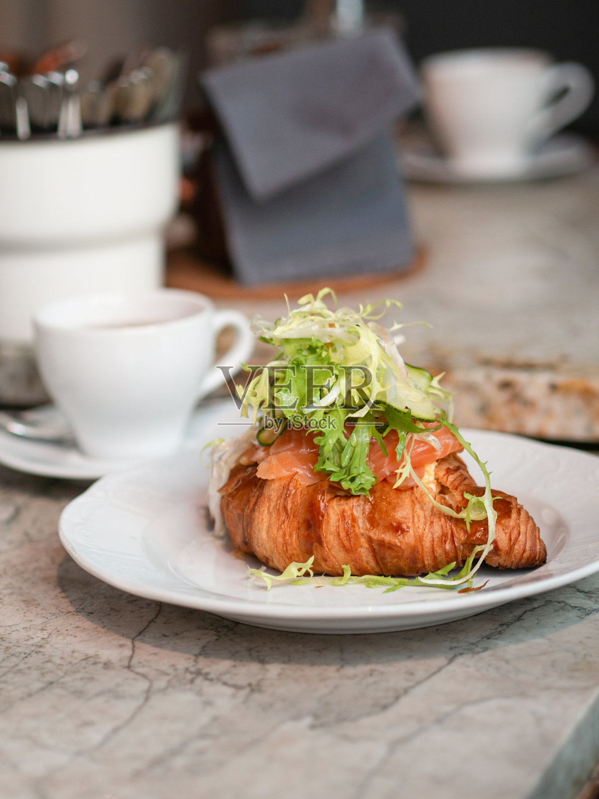 新鲜的牛角面包配三文鱼和生菜，盛在餐桌上的盘子里。照片摄影图片
