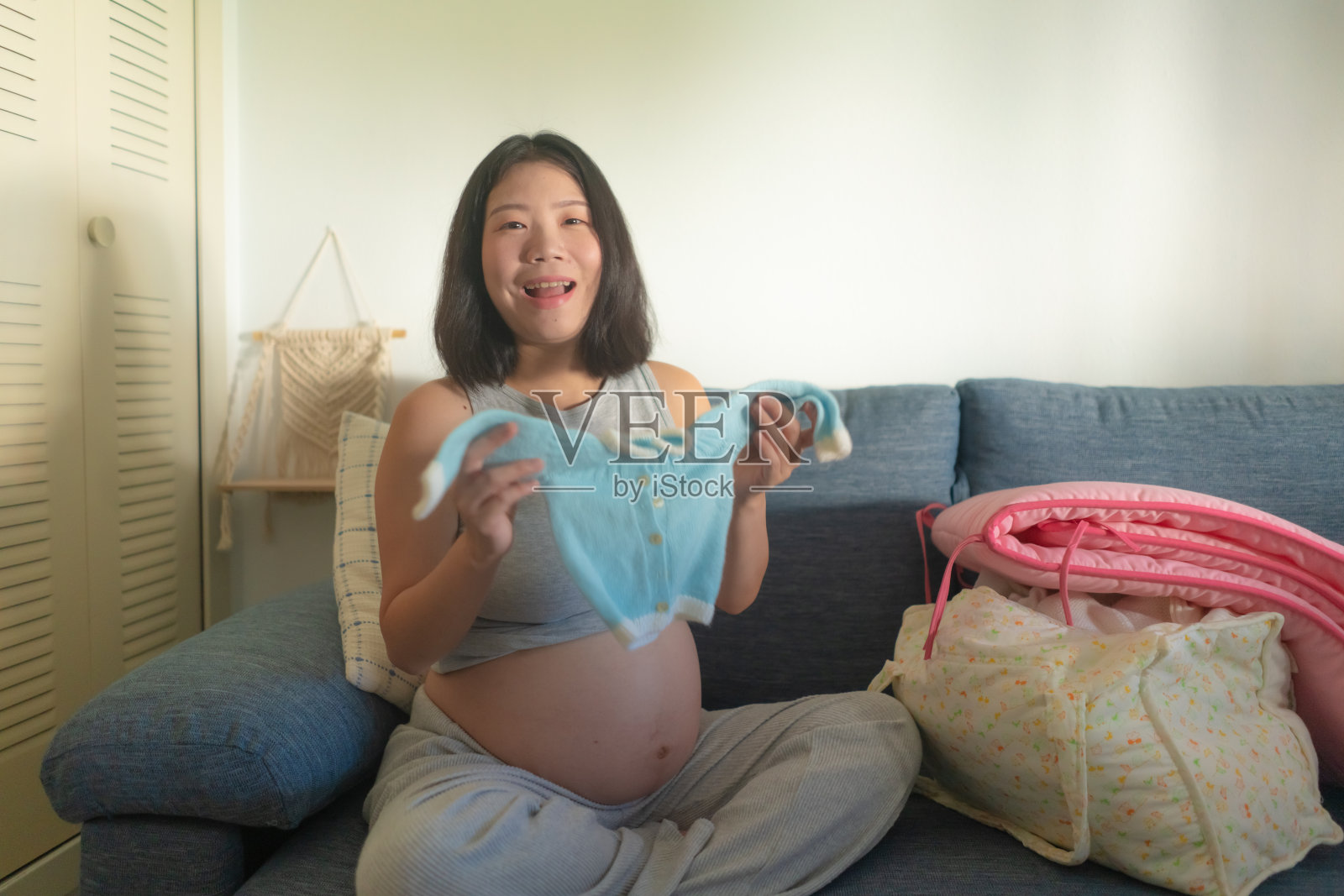 年轻快乐和美丽的亚洲中国妇女怀孕在沙发上顽皮的小婴儿衣服微笑轻松的怀孕和孕妇的概念照片摄影图片