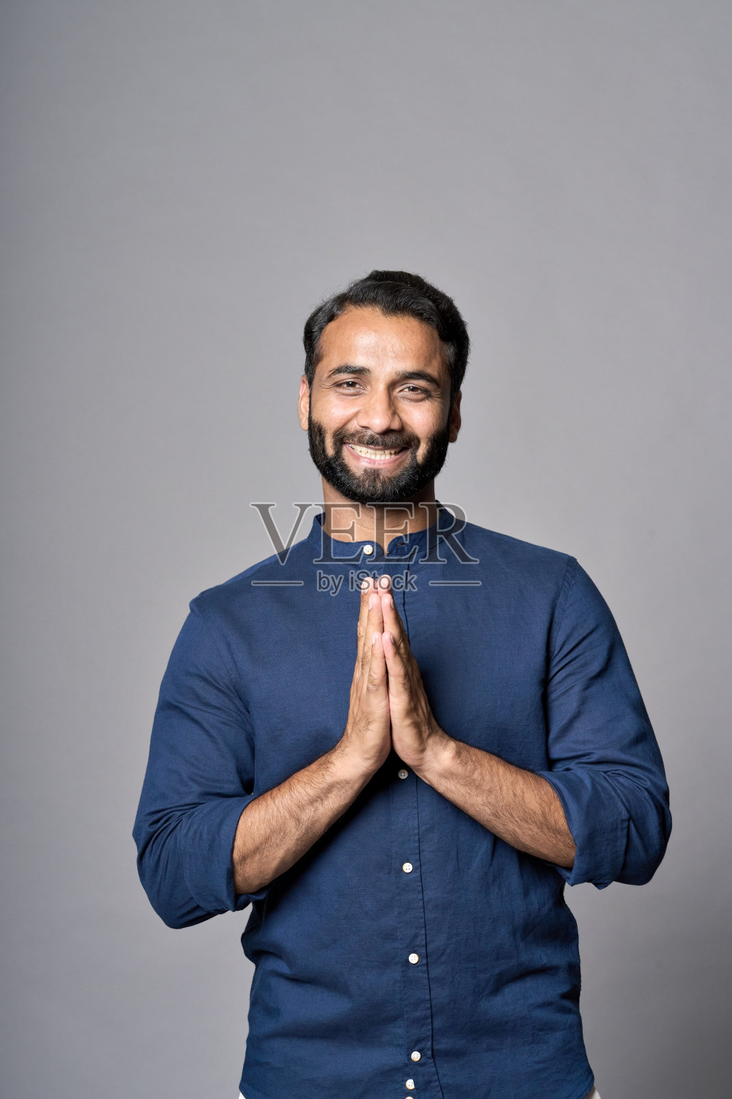 快乐的印度男子冥想，双手合十，在灰色背景中隔离。竖版照片摄影图片