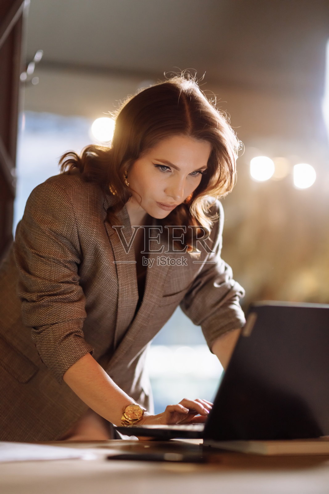 成功美丽的年轻女商人在咖啡馆工作在黄昏。在大窗户旁边的优雅室内，一位女士正在使用笔记本电脑远程工作。照片摄影图片