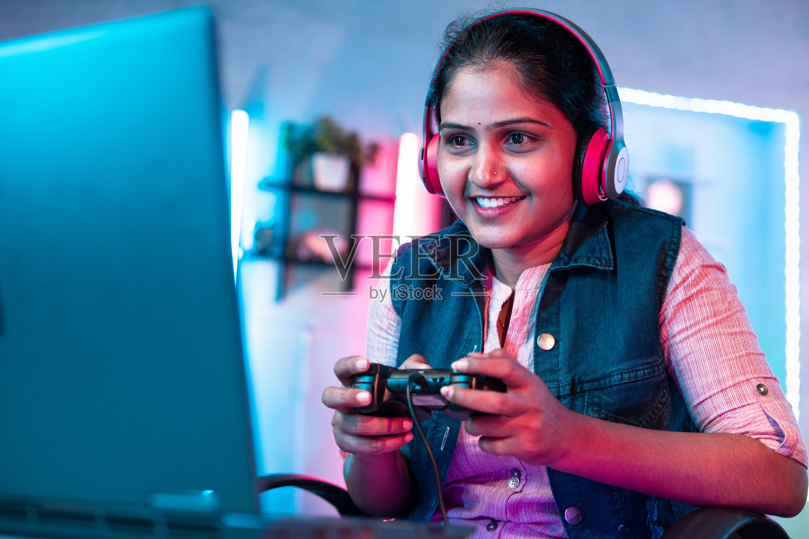 自信的女孩戴着耳机在笔记本电脑上玩电子游戏，在家里使用操纵杆-休闲活动的概念，网络空间和娱乐照片摄影图片