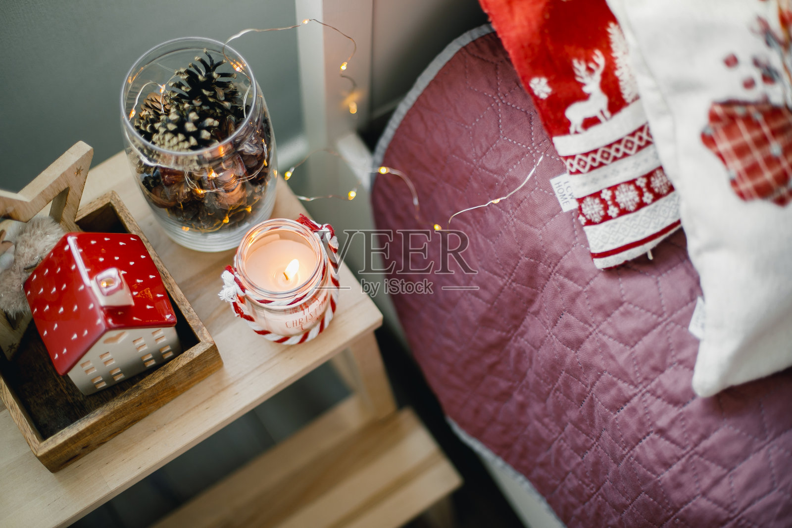 节日装饰。燃烧的蜡烛，陶瓷的房子，坛子上的木锥在床头柜上照片摄影图片