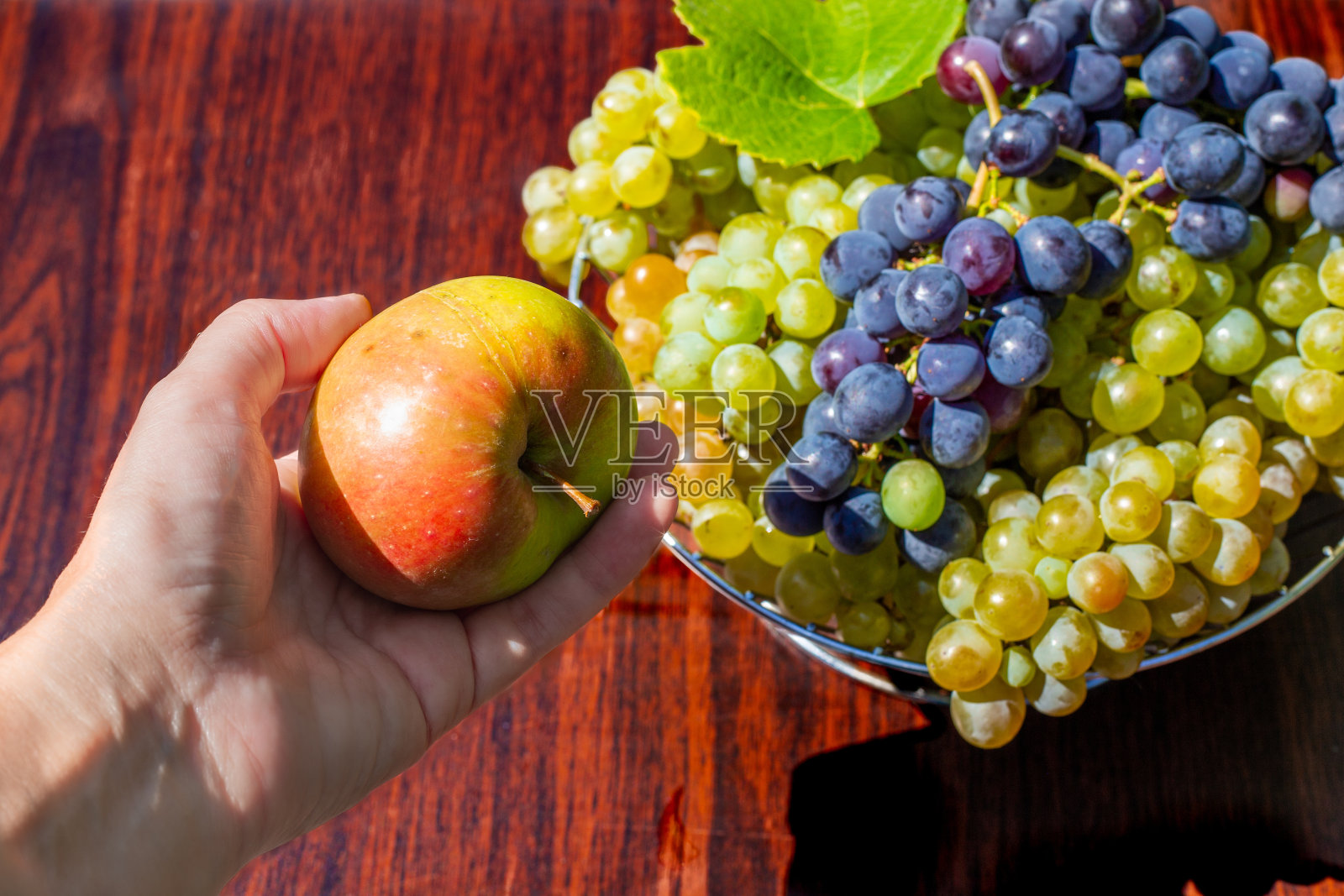 桌上放着葡萄的花瓶，女人手里拿着苹果。美味健康的水果食品照片摄影图片