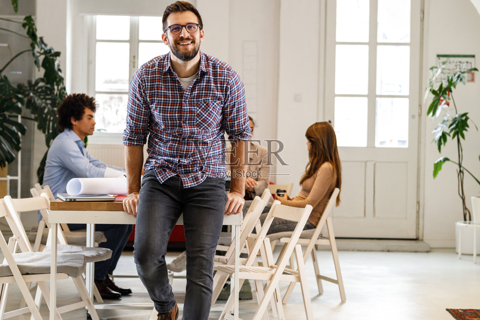 穿着随意的非裔美国商人的肖像坐在他的办公室的桌子上。照片摄影图片