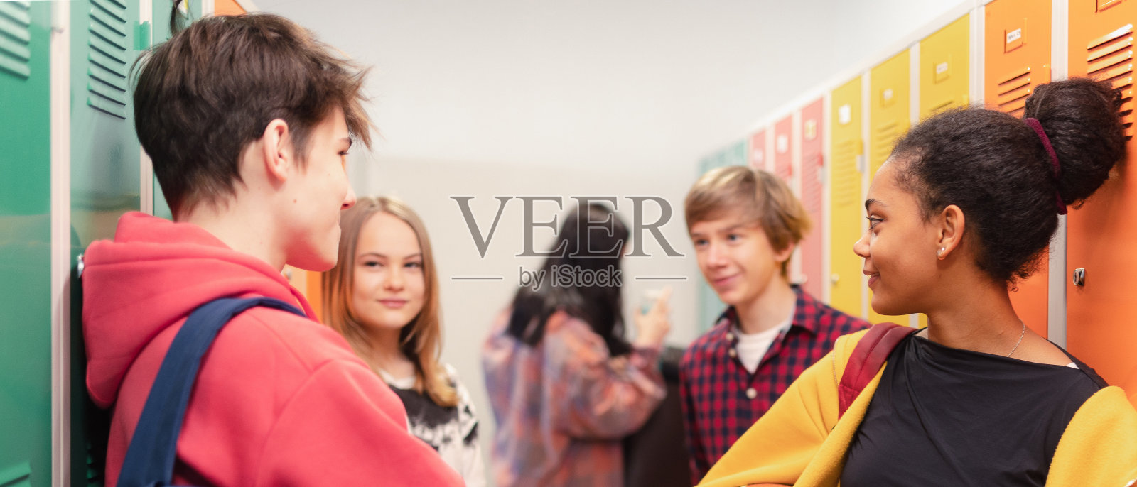 年轻的高中生在校园走廊的储物柜附近见面和打招呼，回到学校的概念。照片摄影图片