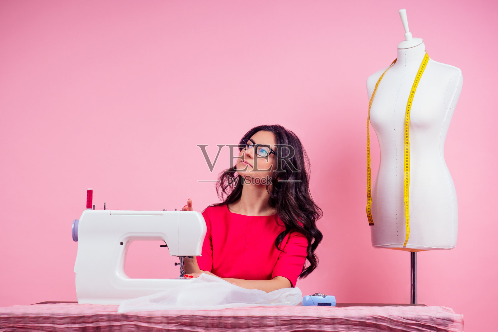 缝纫模式，缝纫机和人体模型在工作室粉红色的背景。裁缝曲线模板。裁缝创造了一个集合，在车间缝制衣服。年轻的女设计师服装笔记的想法照片摄影图片
