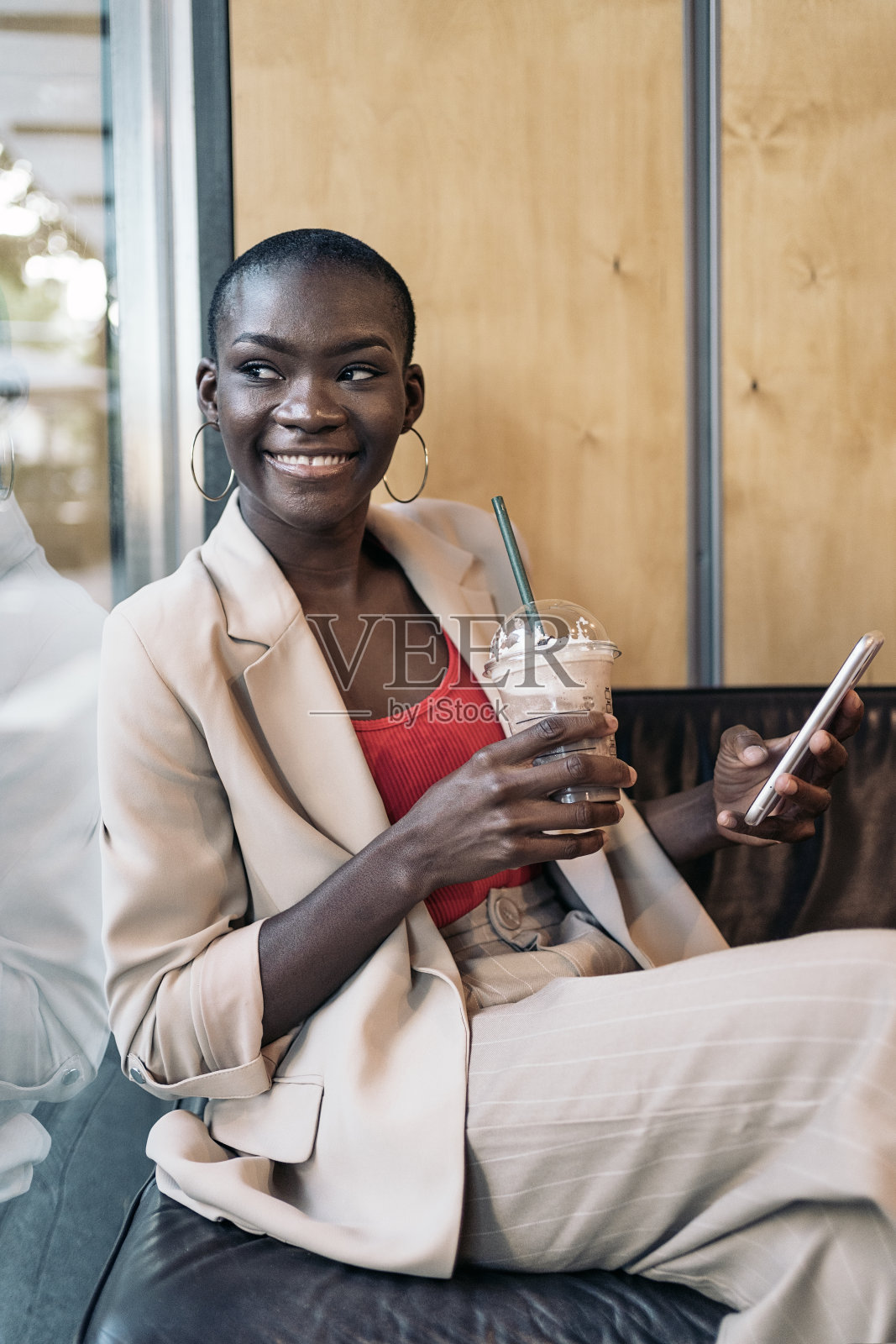 画像一个优雅的年轻女性短发坐在咖啡店喝冰沙透过窗户照片摄影图片