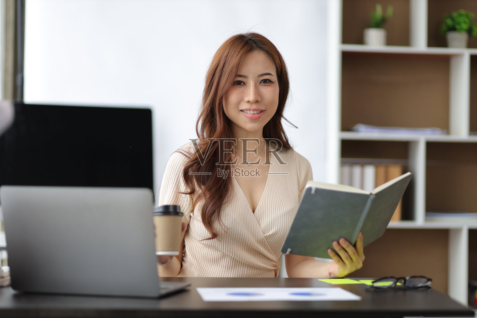 亚洲妇女在办公室桌子上阅读和写笔记本。照片摄影图片