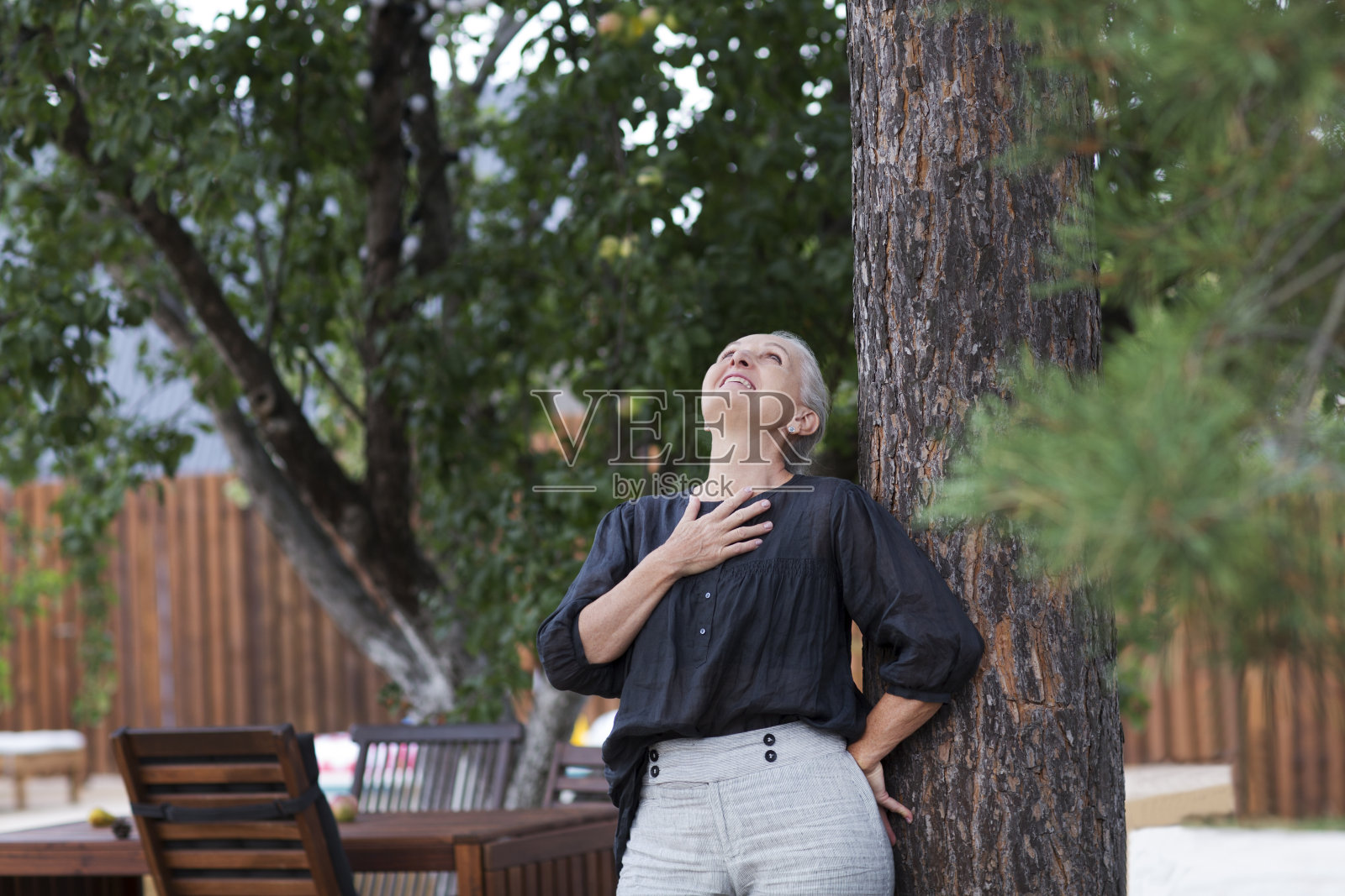 一位成熟的白人妇女站在自家附近的松树旁休息。心理健康。副本的空间。节奏缓慢的生命。享受小事。夏天花时间在大自然中照片摄影图片