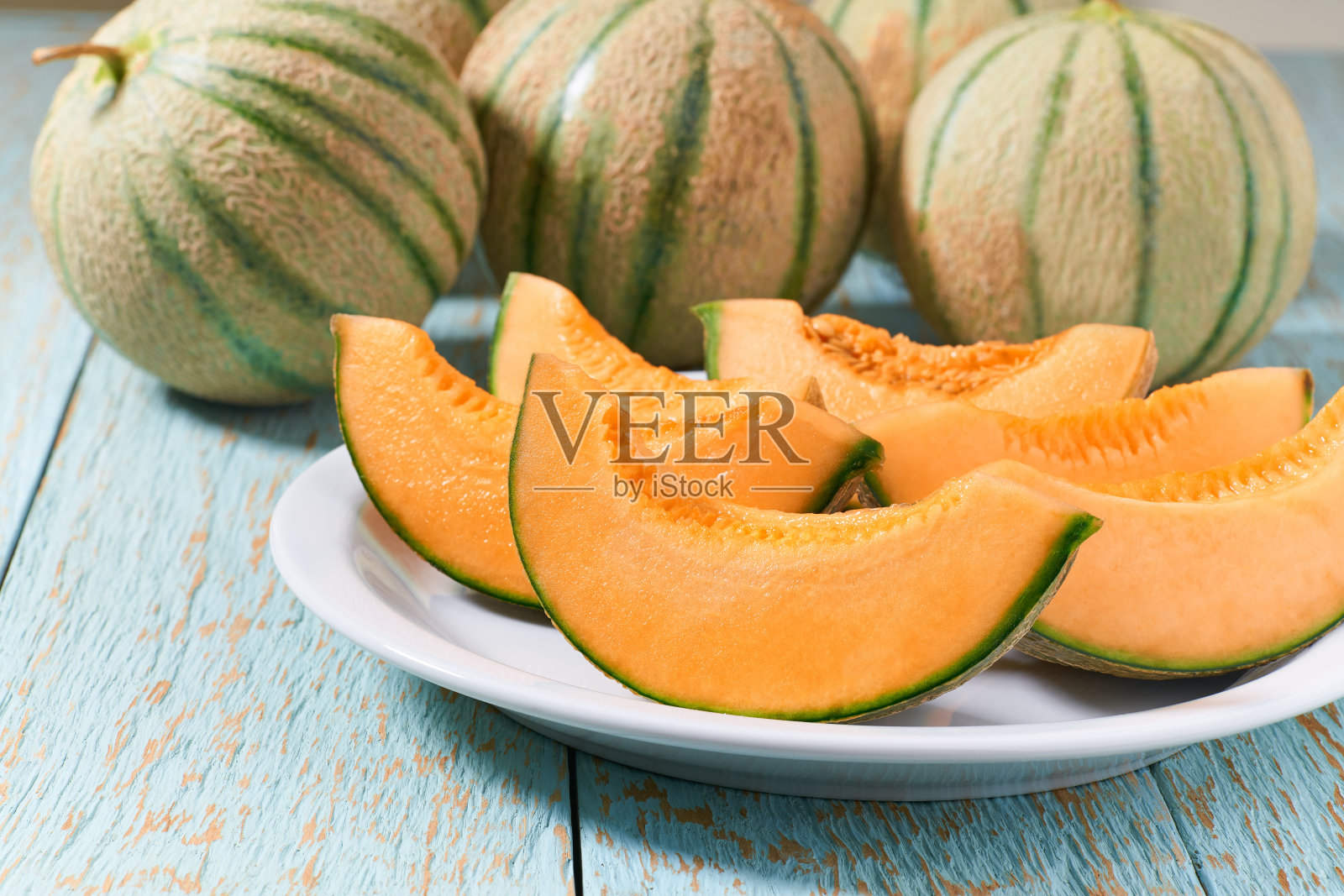 切好的熟瓜装在陶瓷盘里，放在木桌上。照片摄影图片