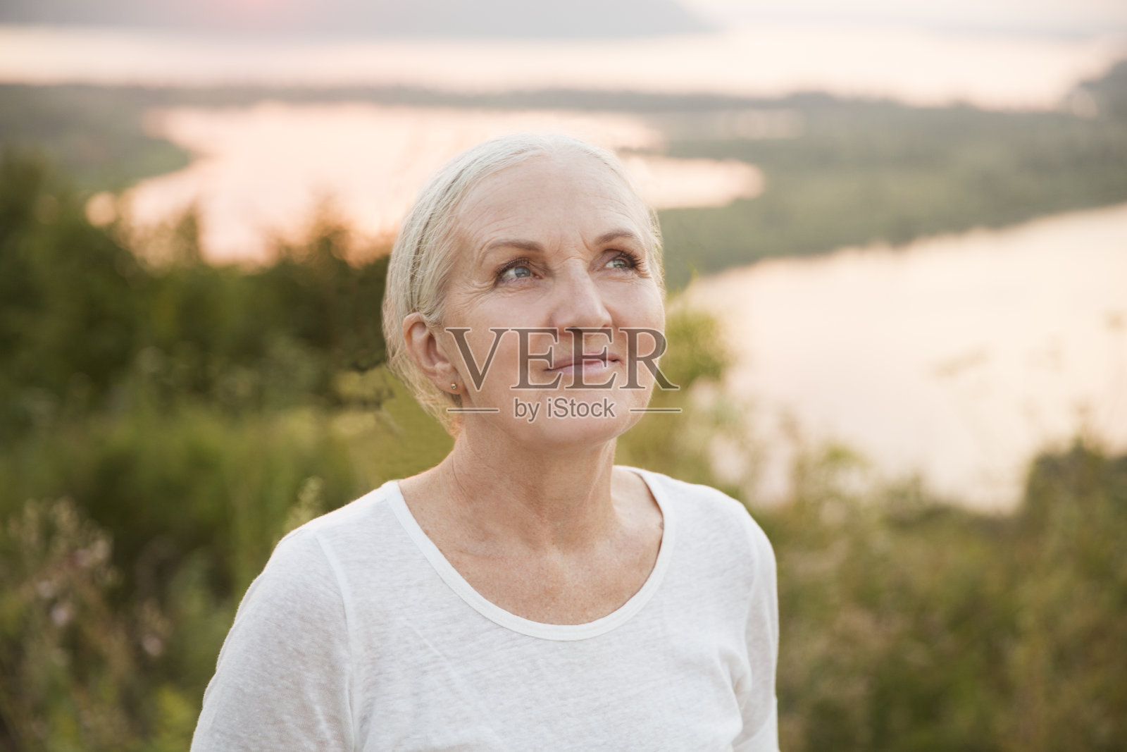 夕阳西下，一名身穿白色t恤、面带微笑的老年妇女放松地看着镜头。副本的空间。节奏缓慢的生命。享受小事。夏天花时间在大自然中照片摄影图片