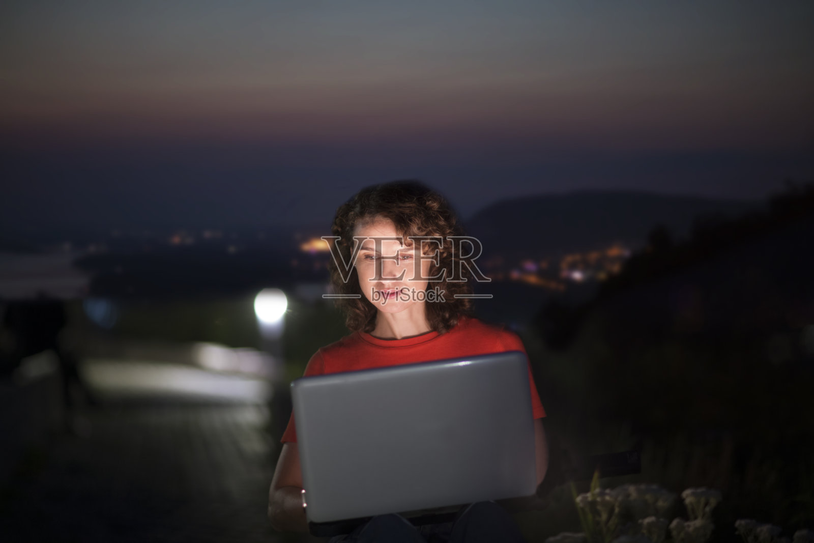 在假期工作，远程工作者。中年妇女使用笔记本电脑，连接到互联网在夏天的城市日落。从任何地方工作。照片摄影图片