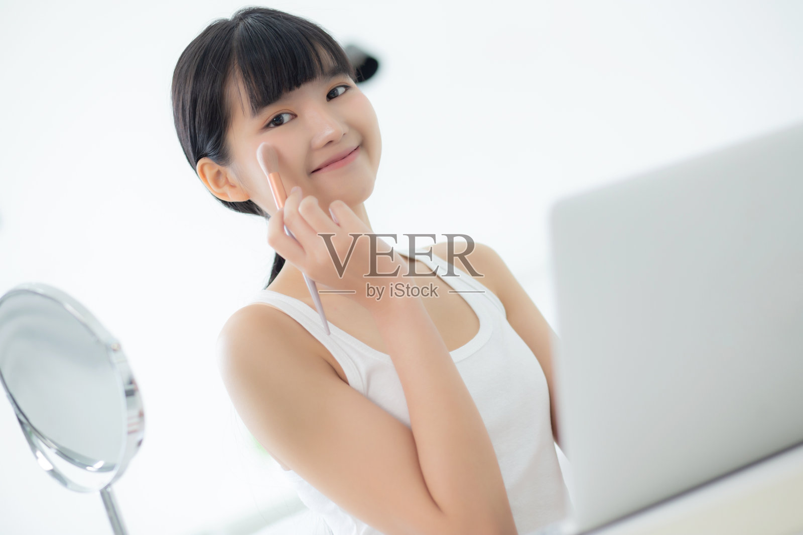 美丽的年轻亚洲女性与学习化妆用刷子在笔记本电脑上的脸颊与在线教程课程，女性教学和解释化妆与社交媒体。照片摄影图片