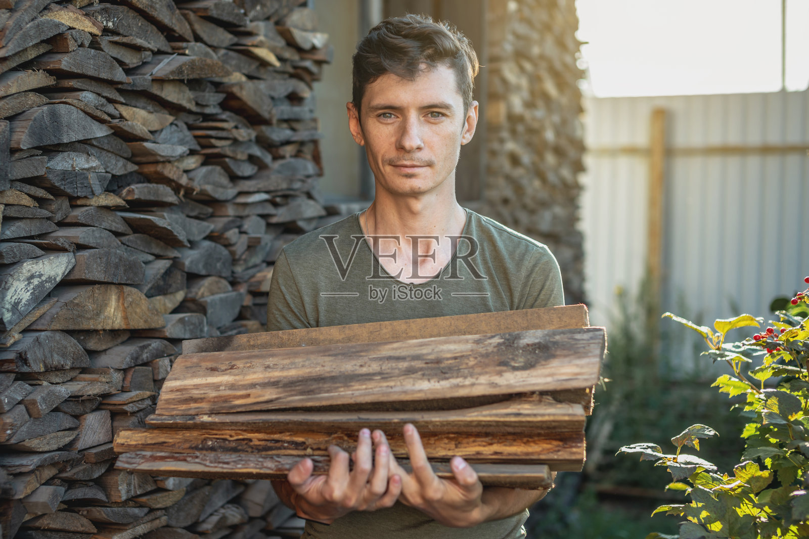 一名男子将从柴堆中取出的木柴放在手中，用作家庭壁炉。燃烧木材取暖的概念和能源危机照片摄影图片