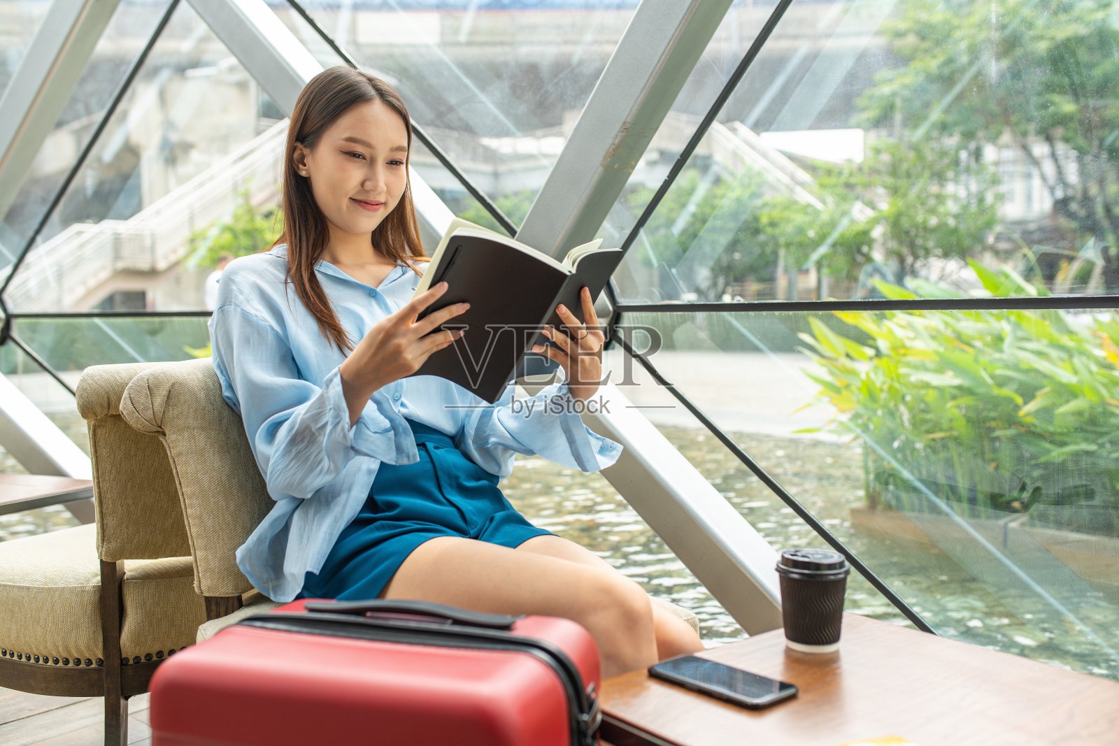 在机场候机楼的咖啡馆里，年轻美丽的亚洲女性独自旅行的女旅行者一边看书一边喝咖啡照片摄影图片