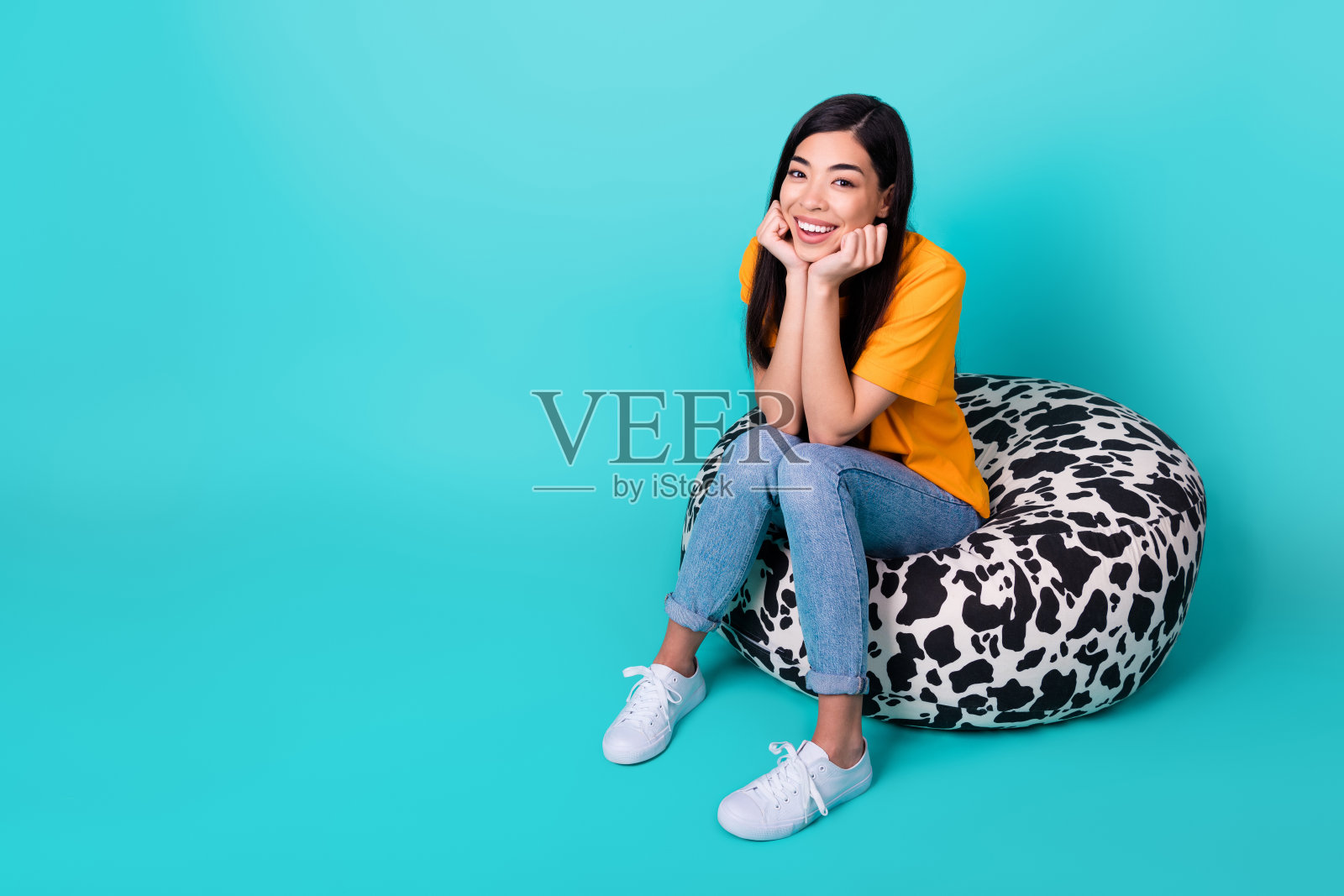 全身照片休息深色女士坐穿t恤牛仔裤运动鞋孤立在蓝绿色的背景照片摄影图片