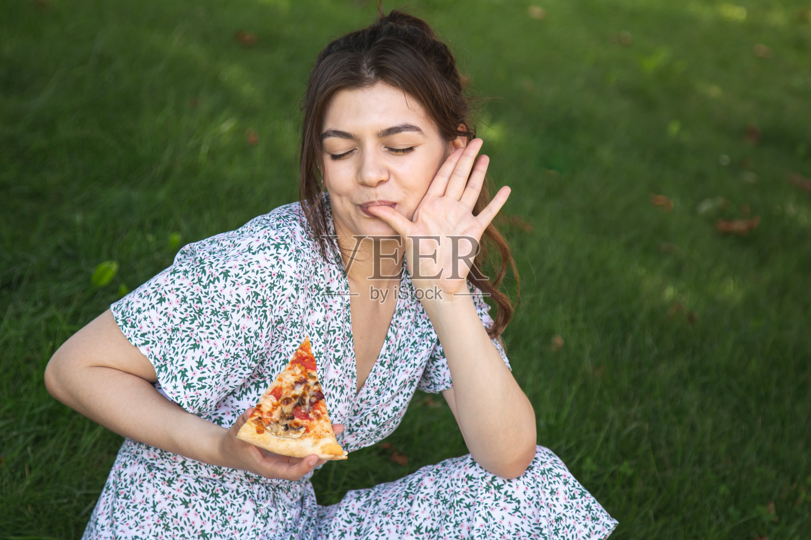 野餐时，一个快乐的年轻女子拿着一块披萨。照片摄影图片