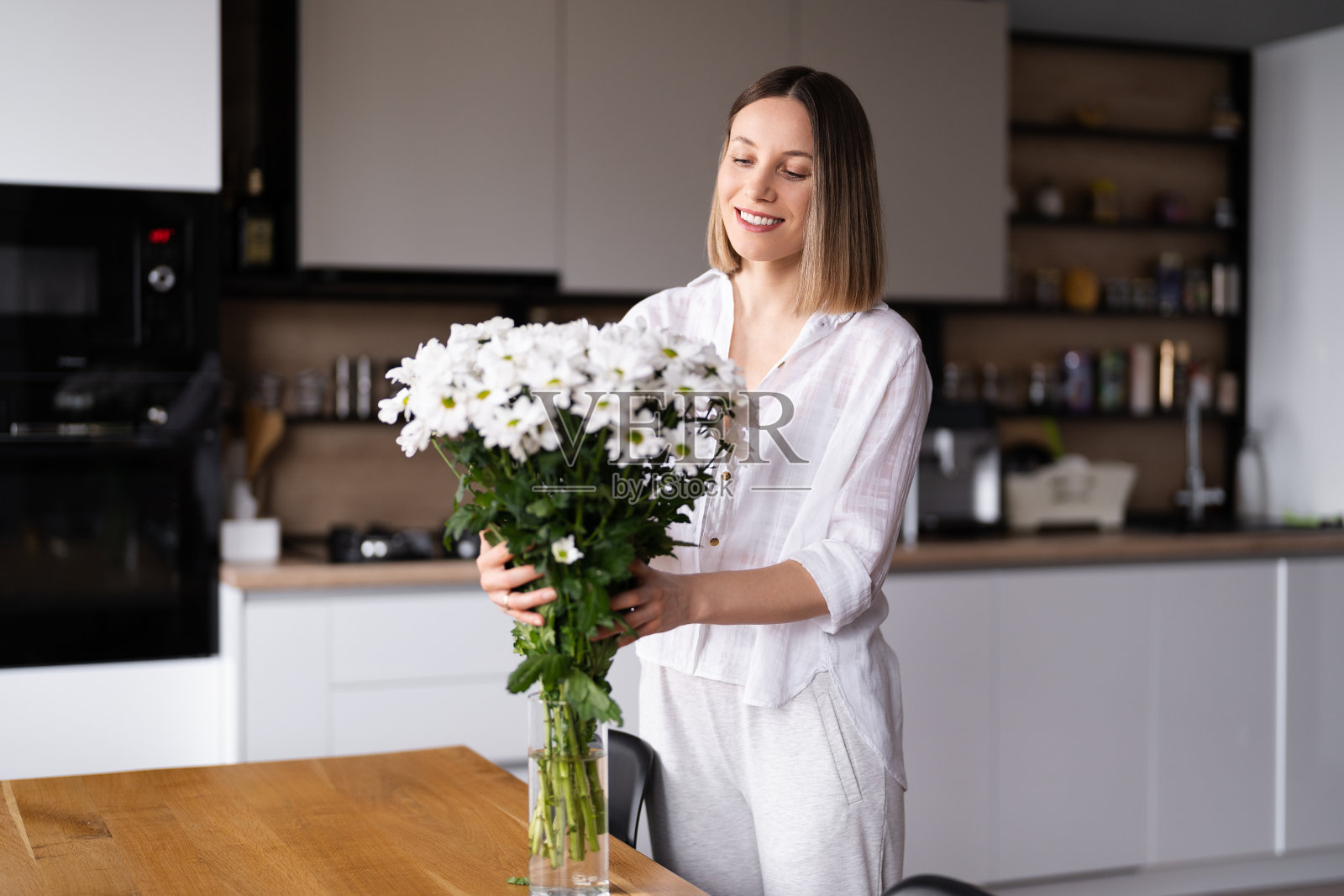 美丽的女人把新鲜的白花放进花瓶里照片摄影图片