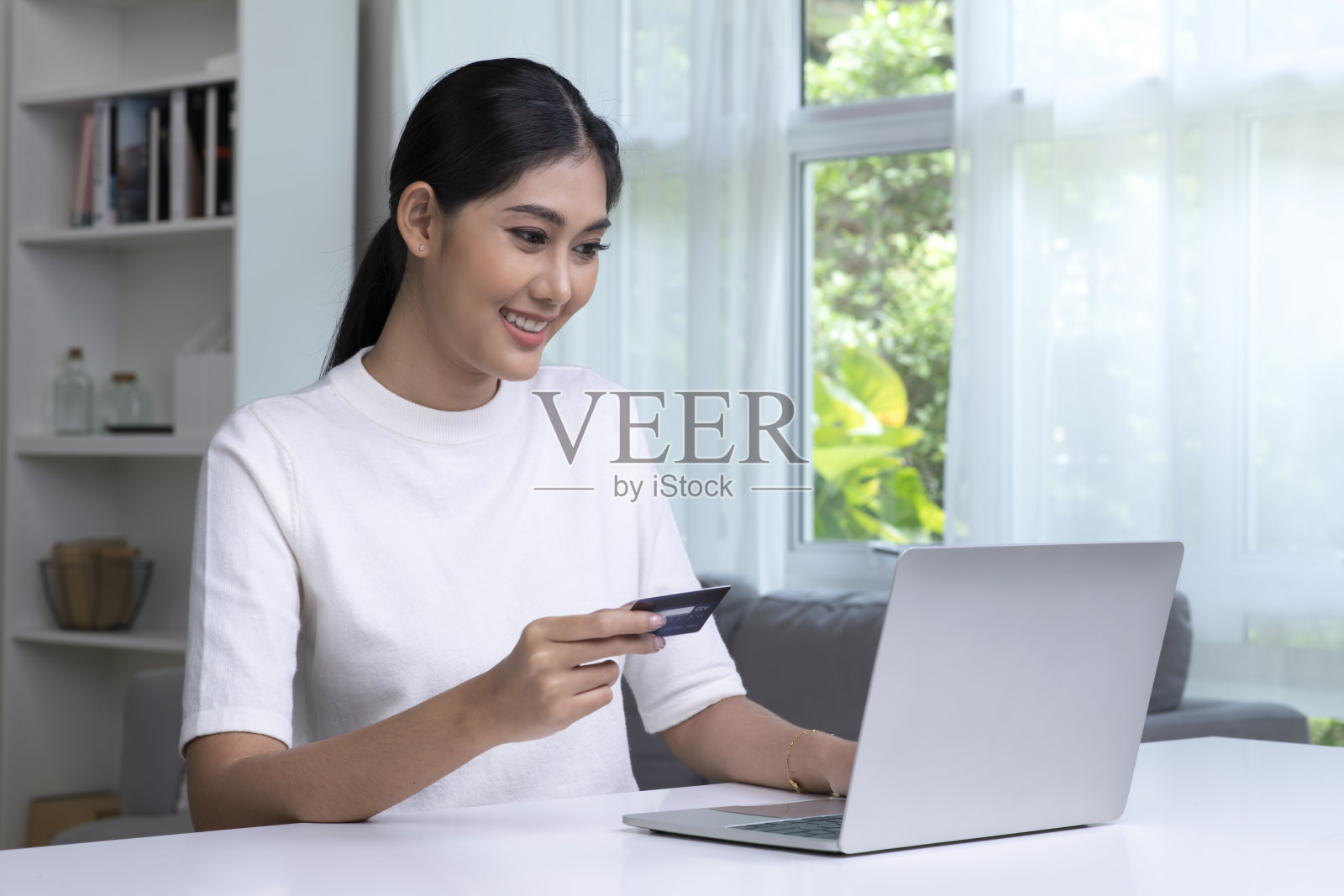 美丽的亚洲女人拿着信用卡，用着笔记本电脑。照片摄影图片