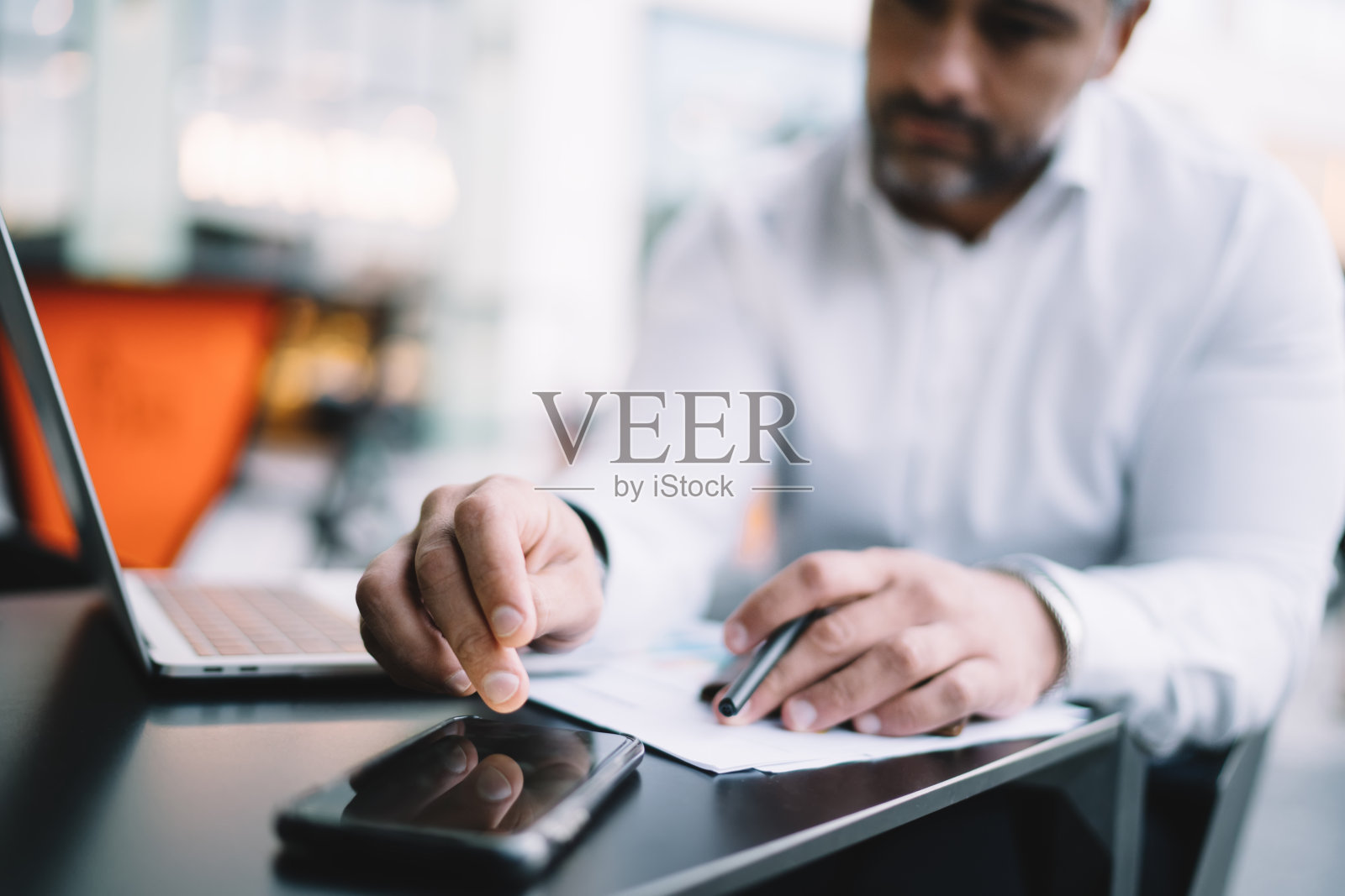 模糊的商人坐在路边的桌子上，使用上网本技术，在移动聊天时使用手机设备检查收到的信息，熟练的男性连接到4g网络进行银行业务照片摄影图片