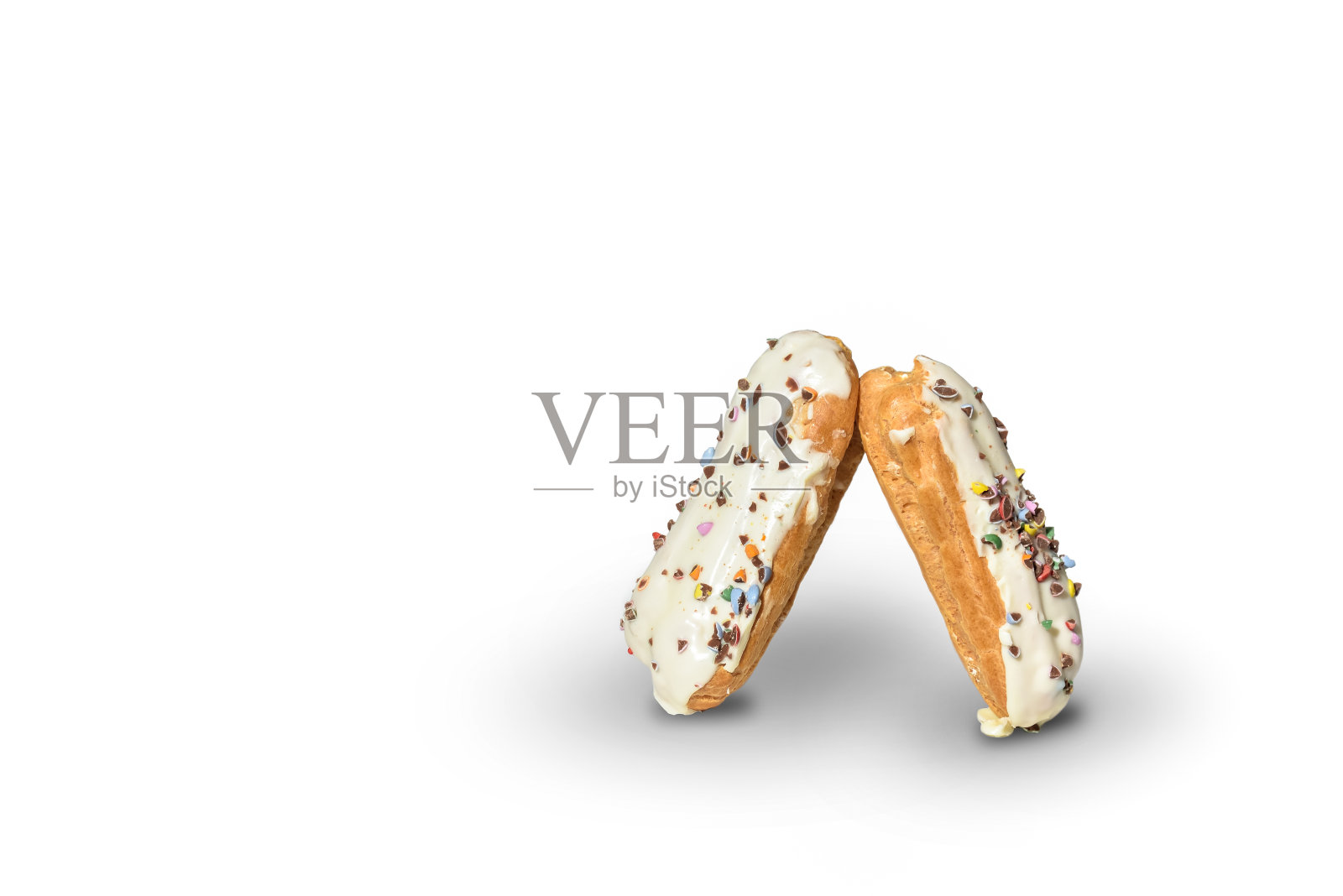 两个用白巧克力糖霜装饰的泡芙，白色背景上点缀着彩色的烘焙粉。照片摄影图片