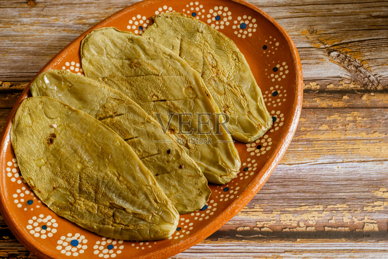 木桌上摆着一个泥盘，上面有nopales。照片摄影图片