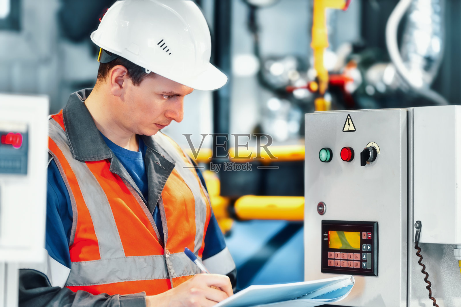 年轻的工程师要在钢盔和防护背心上记录锅炉房设备或气体消耗的日志读数。照片摄影图片