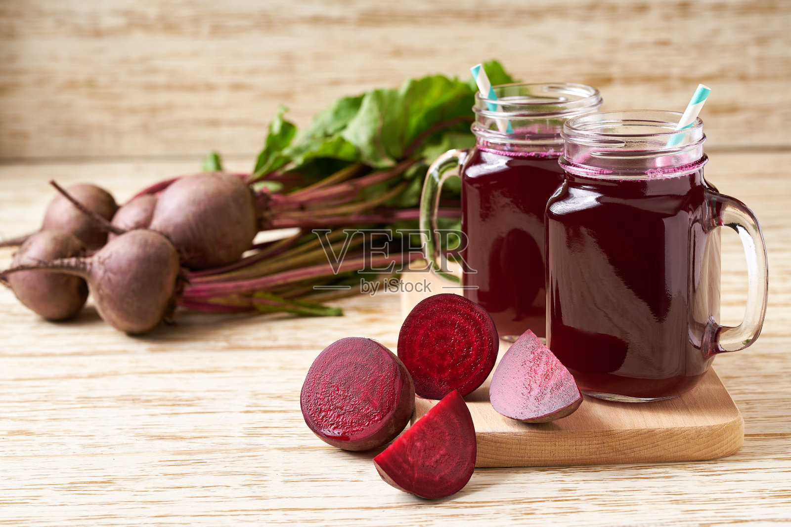 玻璃瓶里盛着新鲜的甜菜汁，木桌上放着蔬菜。照片摄影图片