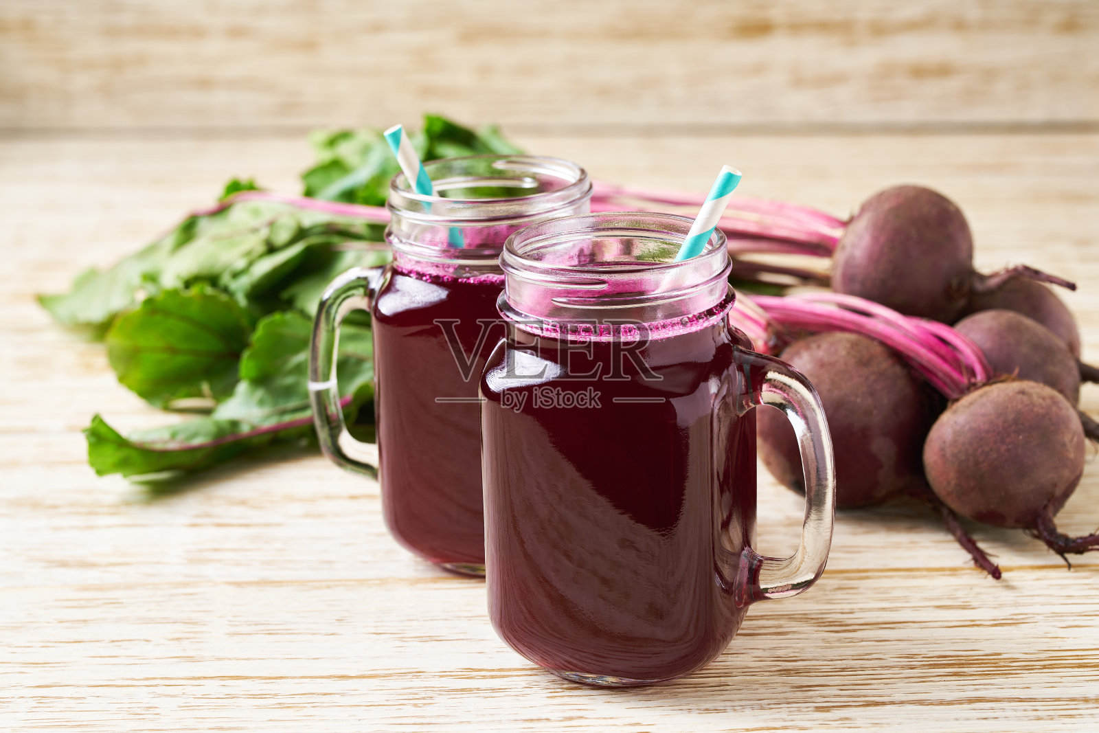 玻璃瓶里盛着新鲜的甜菜汁，木桌上放着蔬菜。照片摄影图片