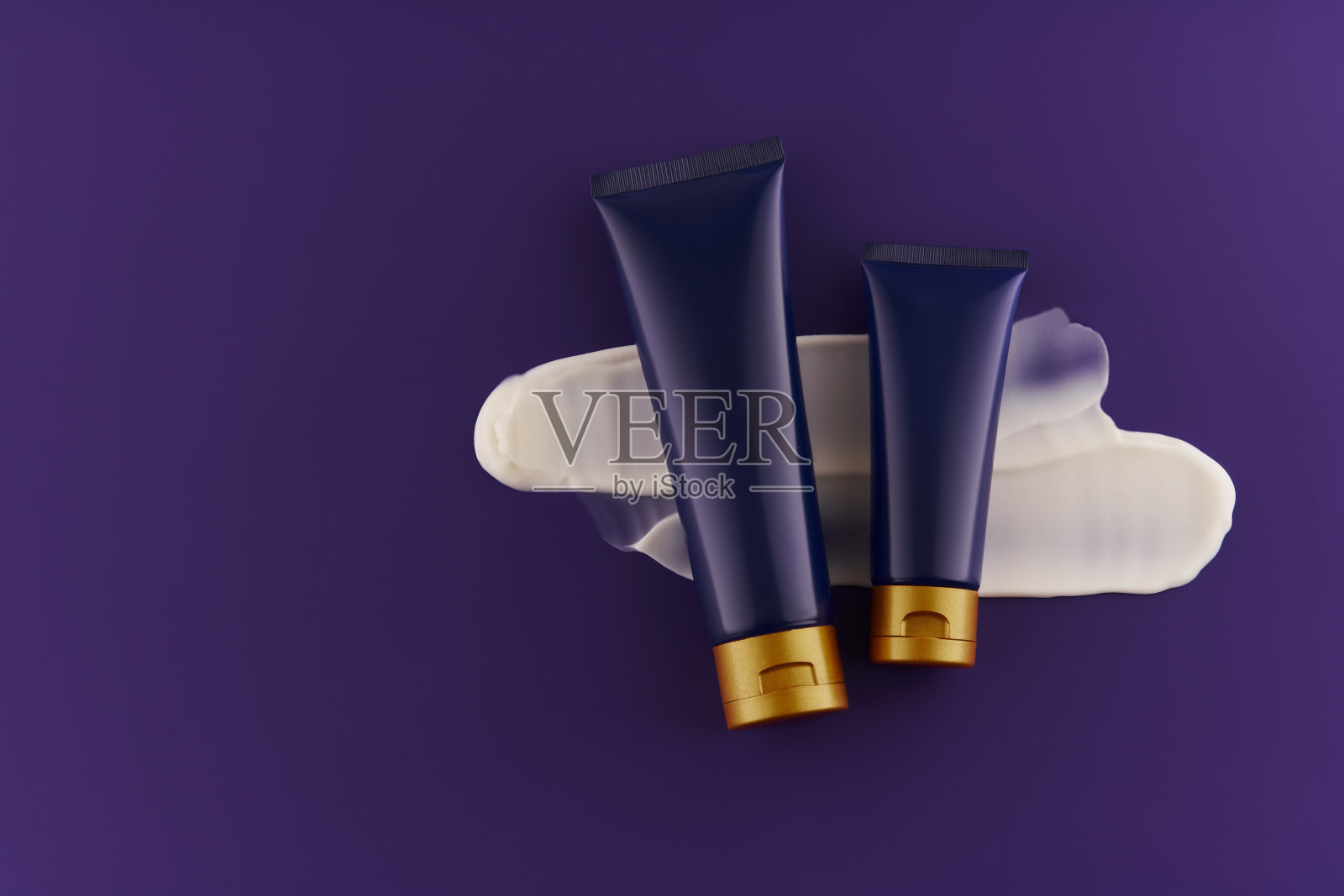 化妆品晚霜管与白色涂片。高级广告。俯视图，紫色背景，蓝色瓶子里的晚霜。照片摄影图片