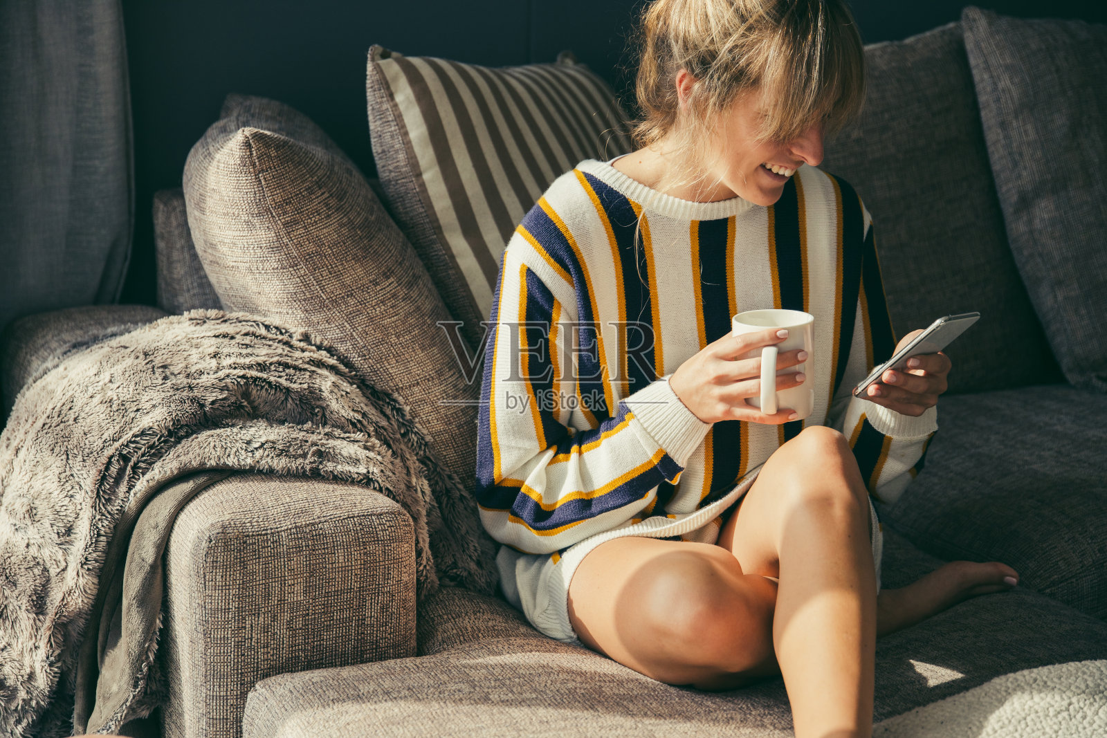 快乐的女人在沙发上喝着咖啡，用着电话照片摄影图片