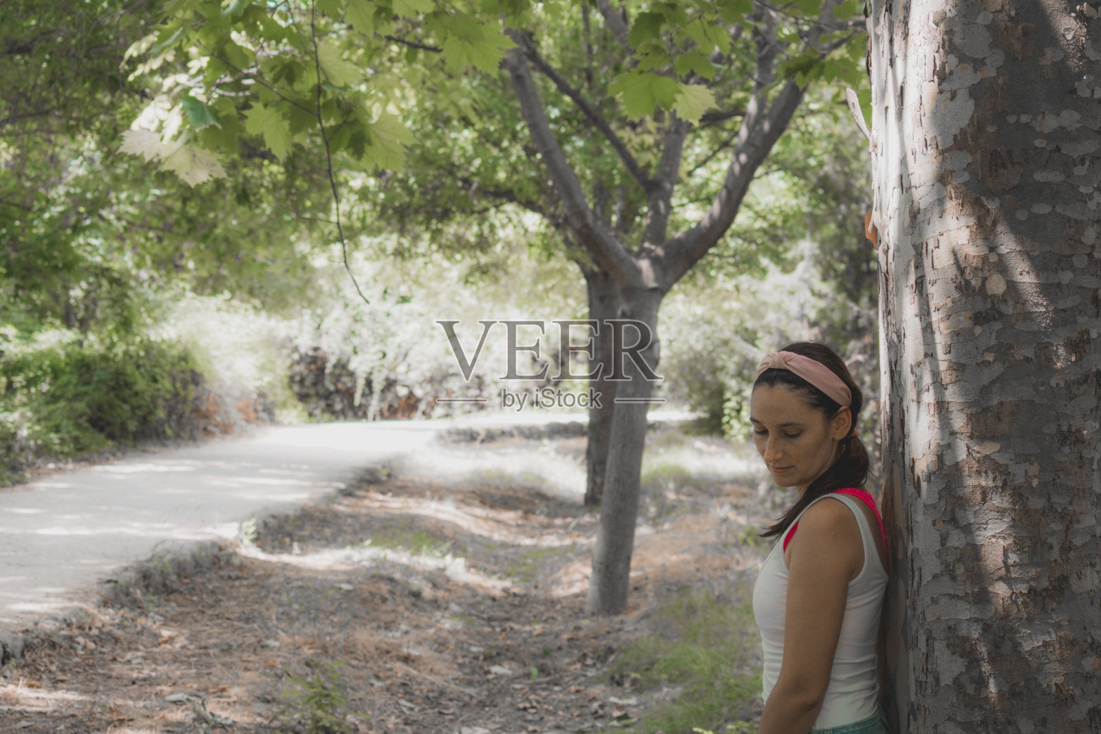 年轻女子靠在树上，看起来很平静照片摄影图片