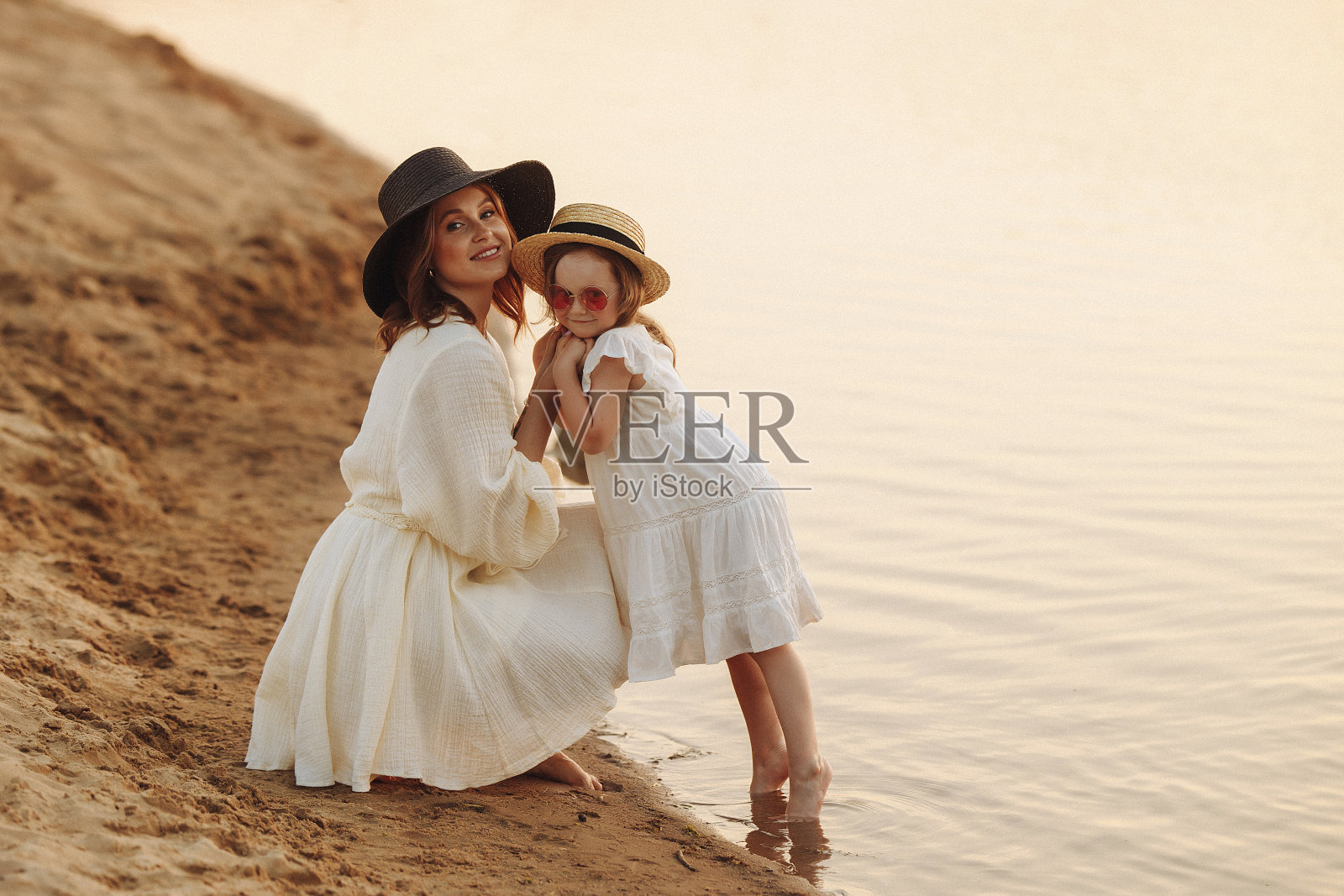 快乐的妈妈和可爱的女儿站在沙滩上。照片摄影图片